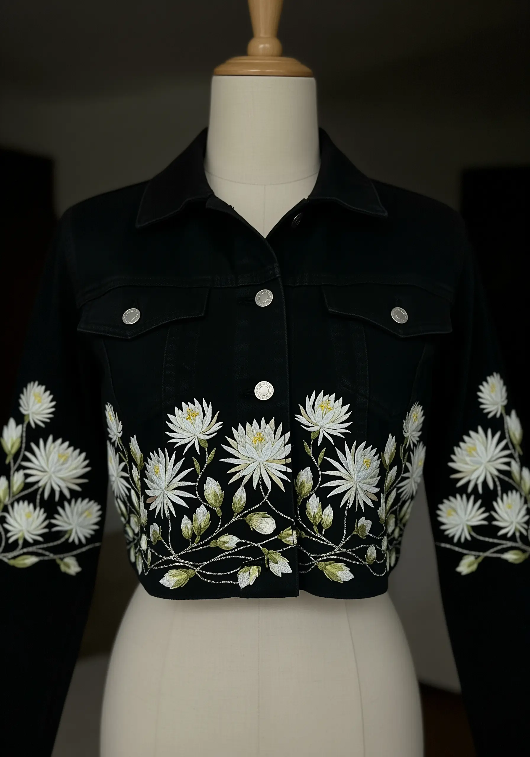 White chrysanthemum embroidery bordering the hem of a cropped black denim jacket.