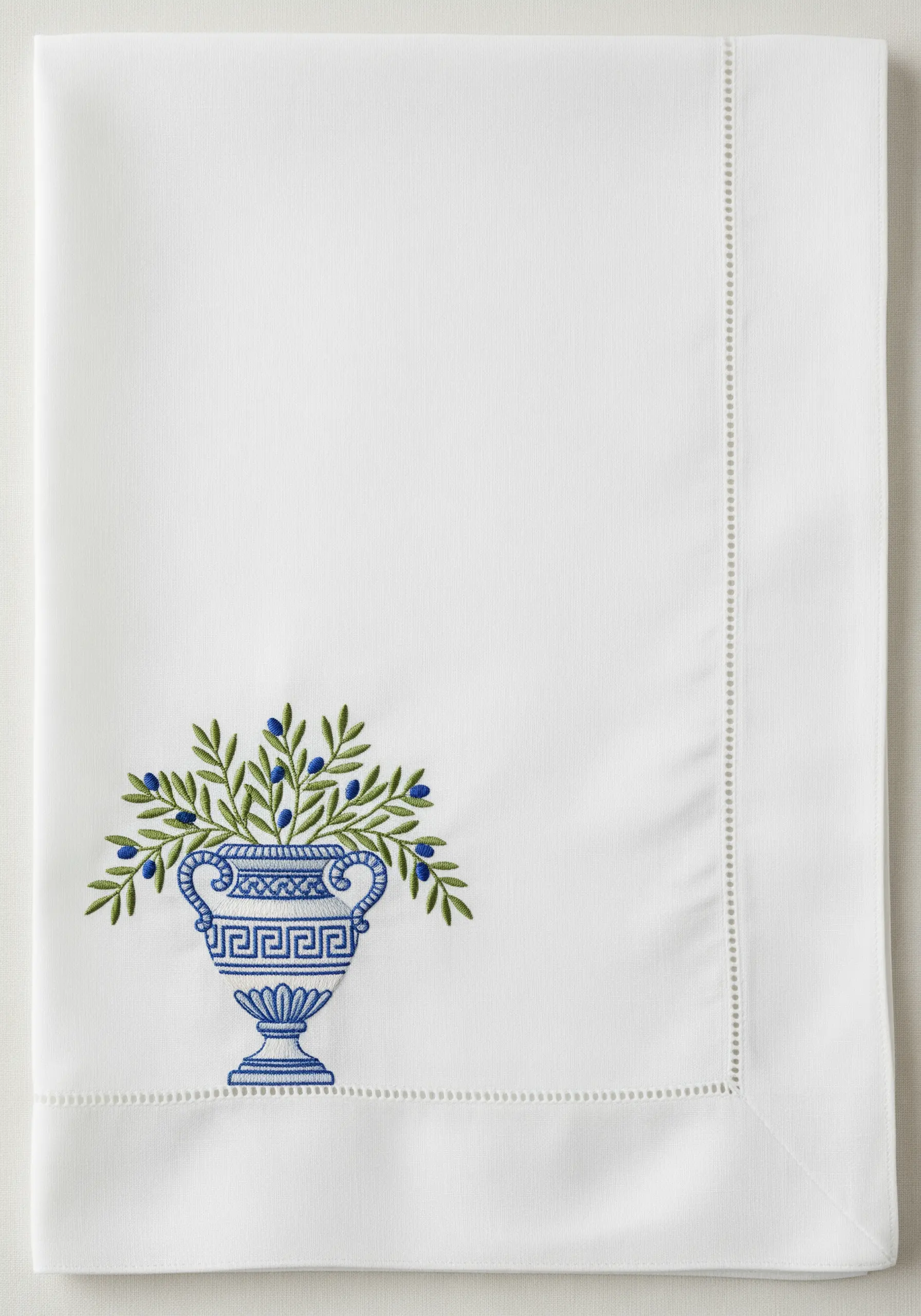 An embroidered Greek urn in blue and white, filled with olive branches.