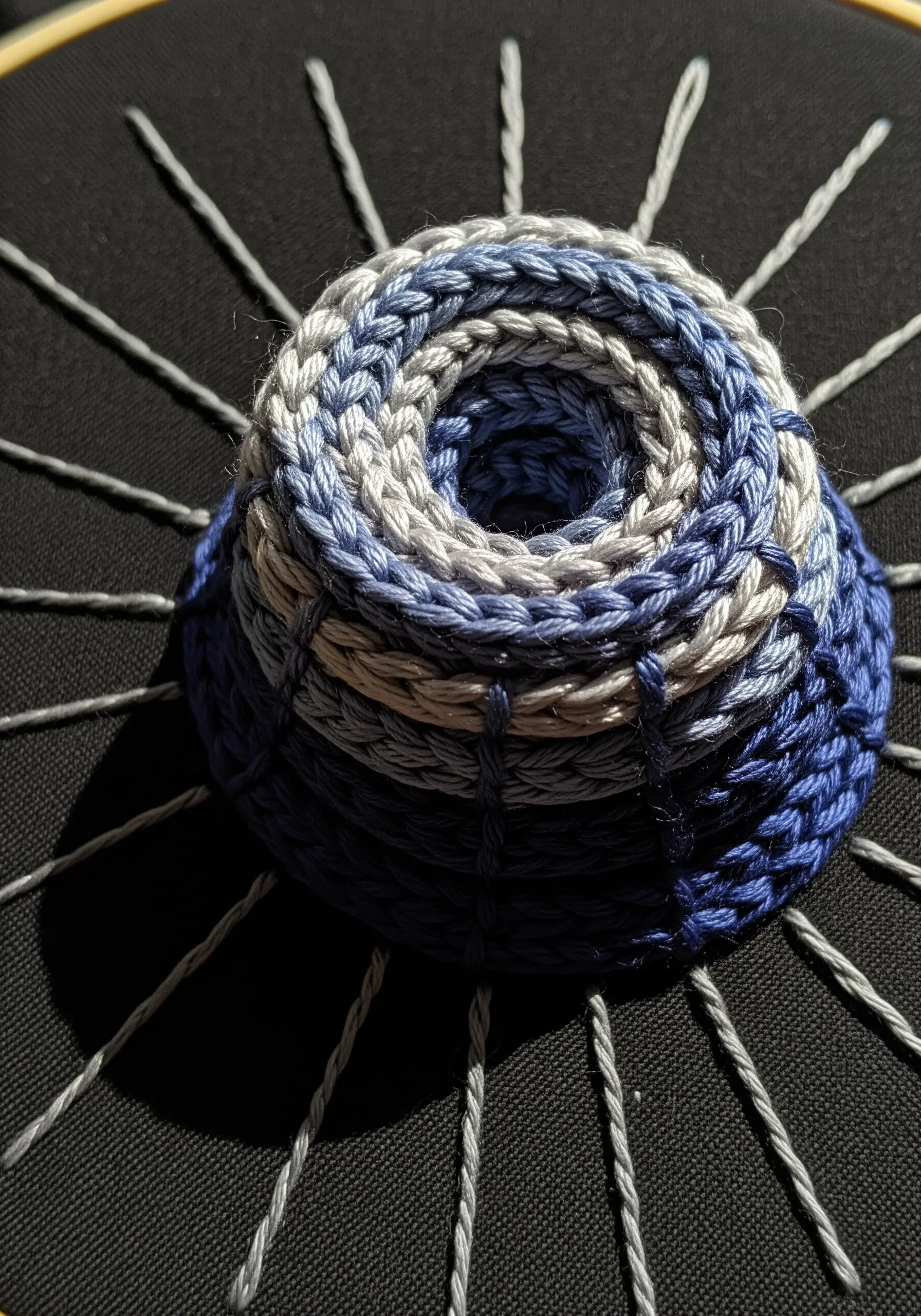 A coiled, basket-like 3D structure in blue gradient threads on black fabric.