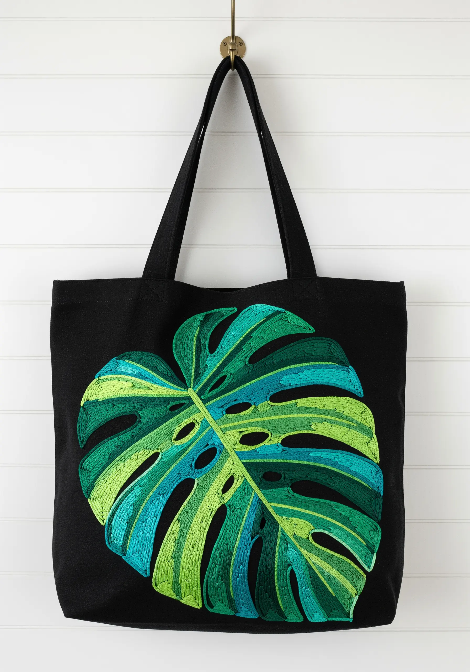 Large, color-blocked Monstera leaf in shades of green and blue on a black tote bag.