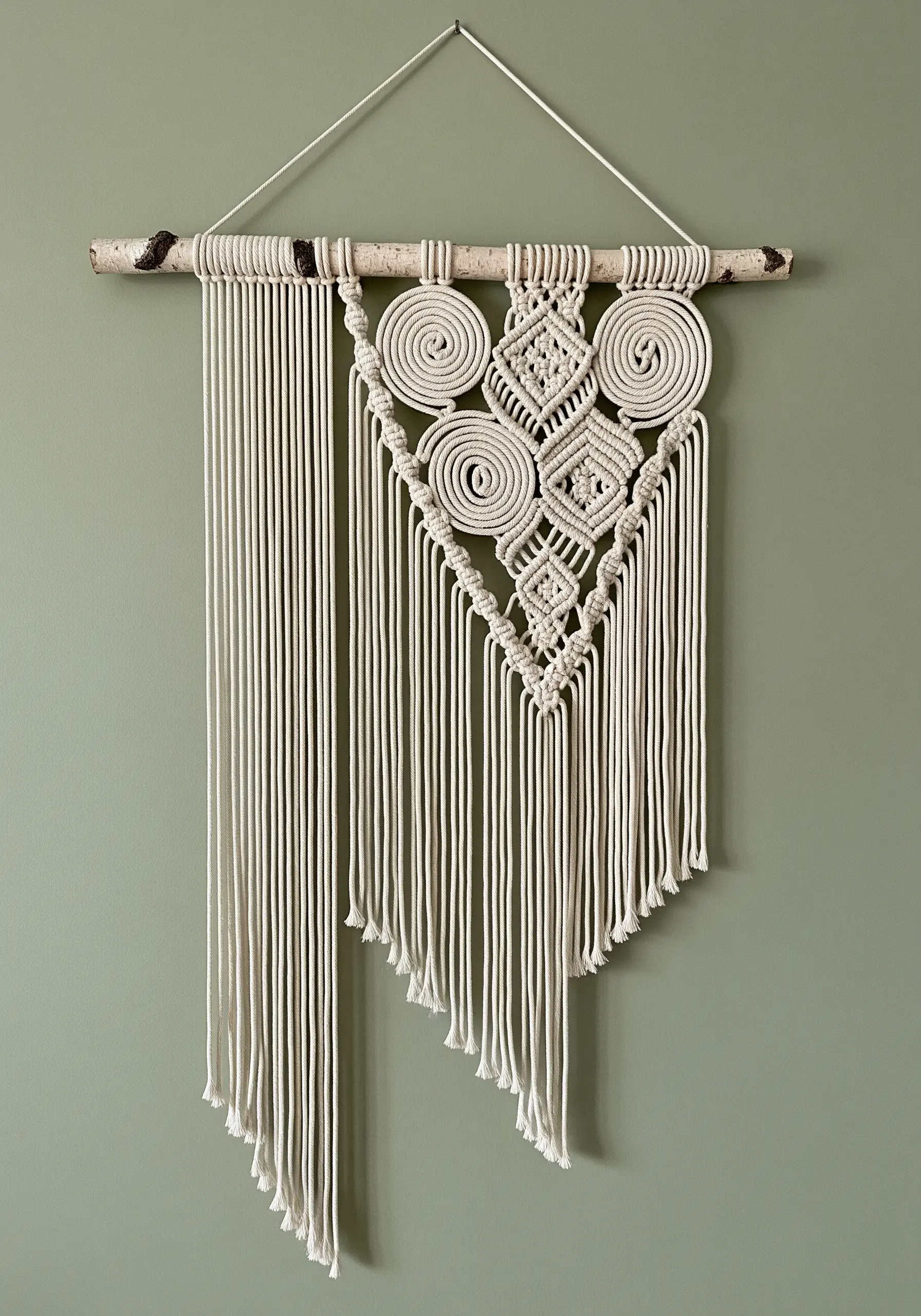 An intricate macrame wall hanging with spiral and diamond patterns, finished with an angled fringe.