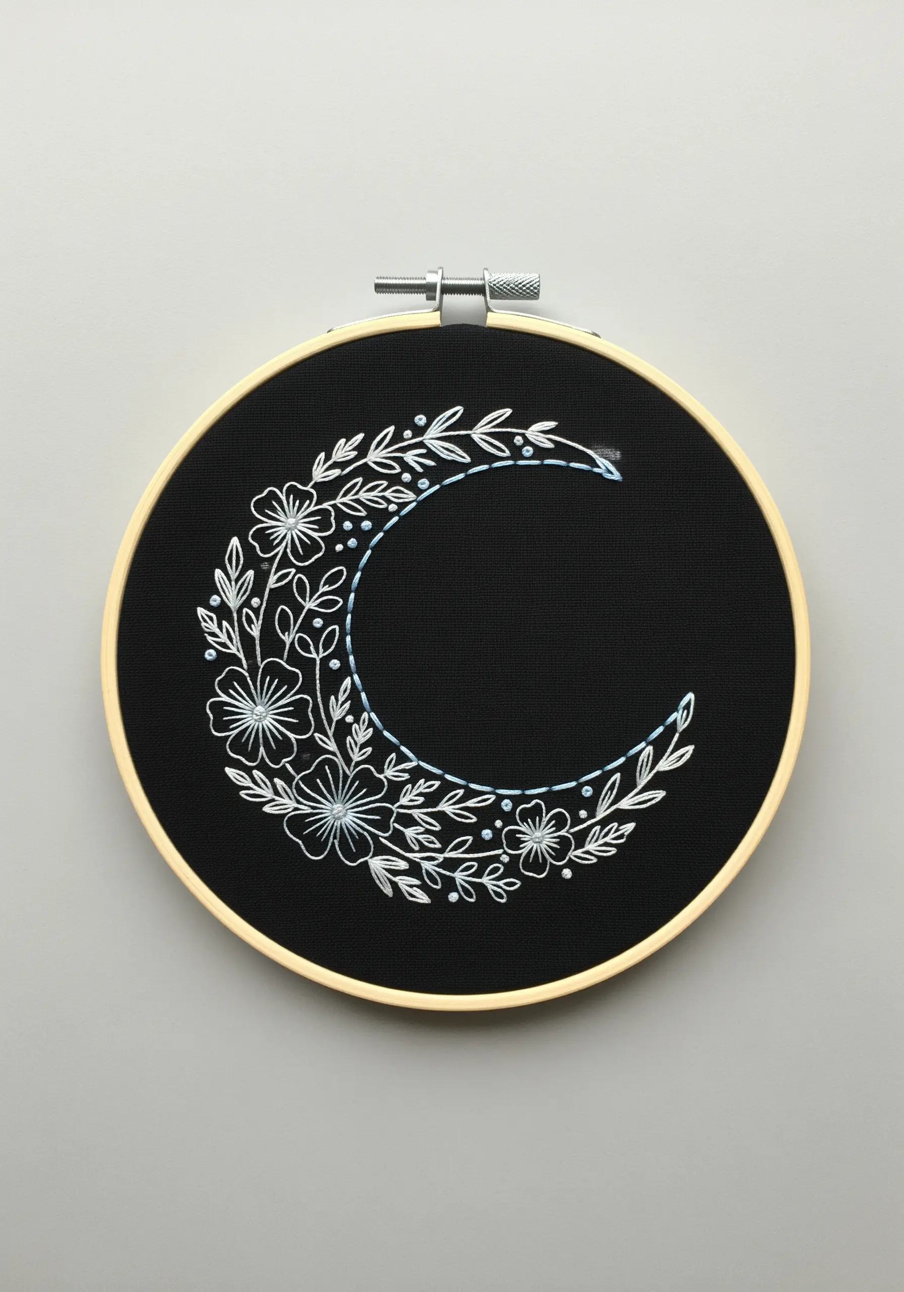 A crescent moon shape filled with white line-art flowers embroidered on black fabric.