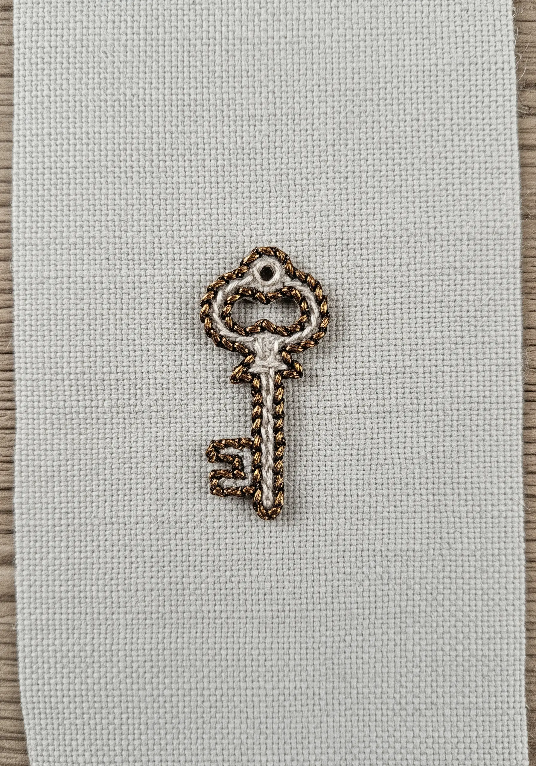 An antique-style key embroidered with a mix of metallic gold and matte white thread.