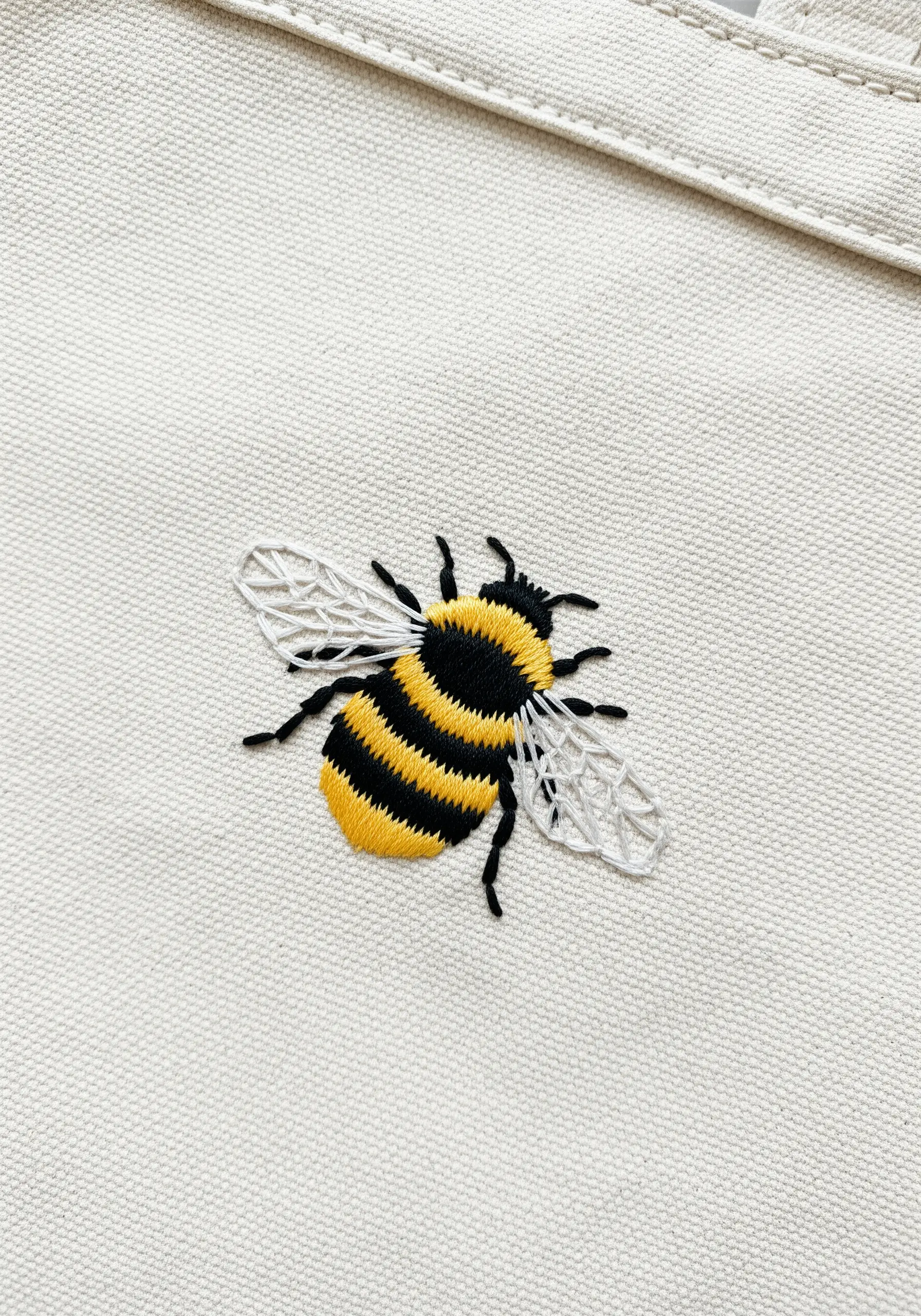 A realistically embroidered bumblebee on a canvas tote bag, showing different textures.