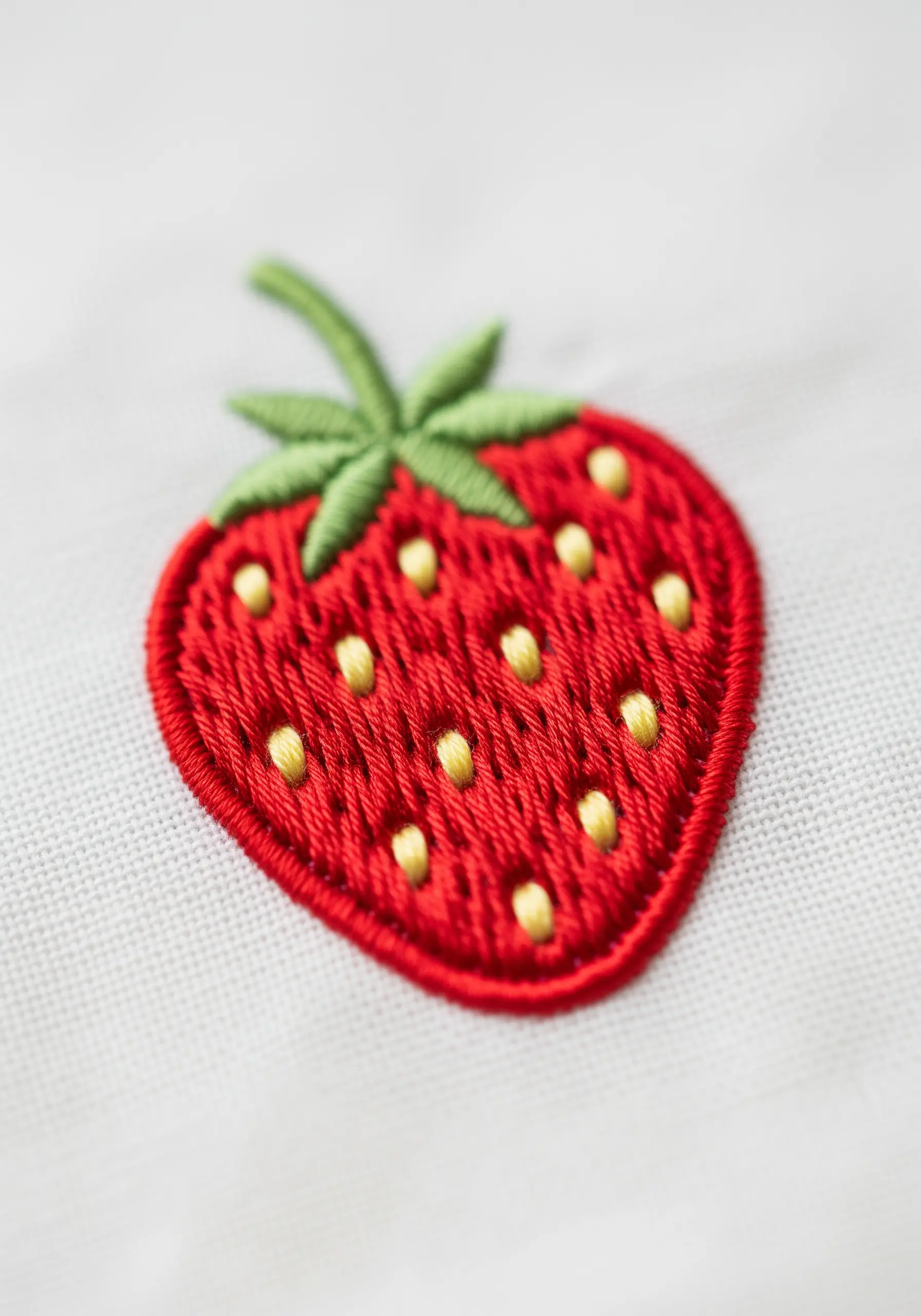 A close-up of a vibrant red embroidered strawberry with yellow French knot seeds.