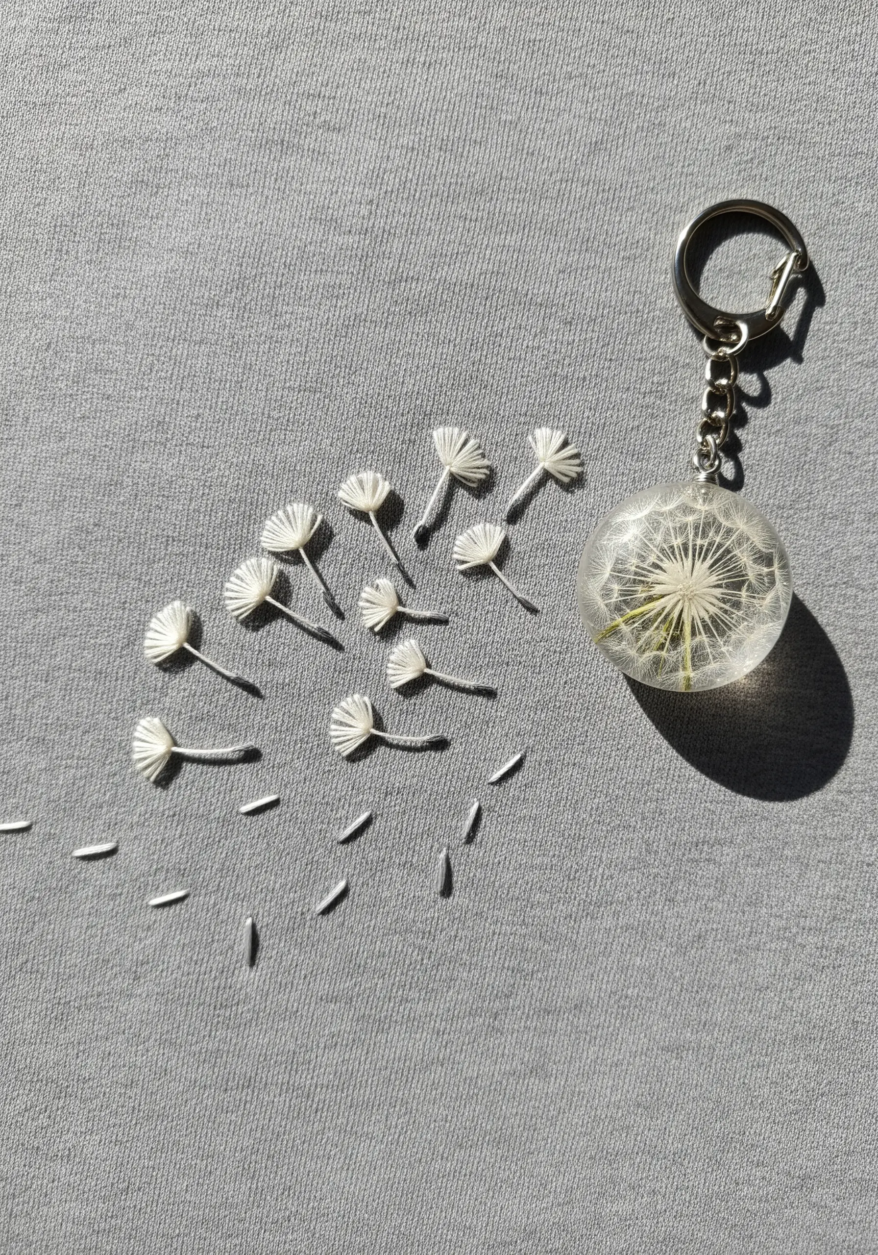 Embroidered dandelion seeds floating towards a resin orb with a real dandelion