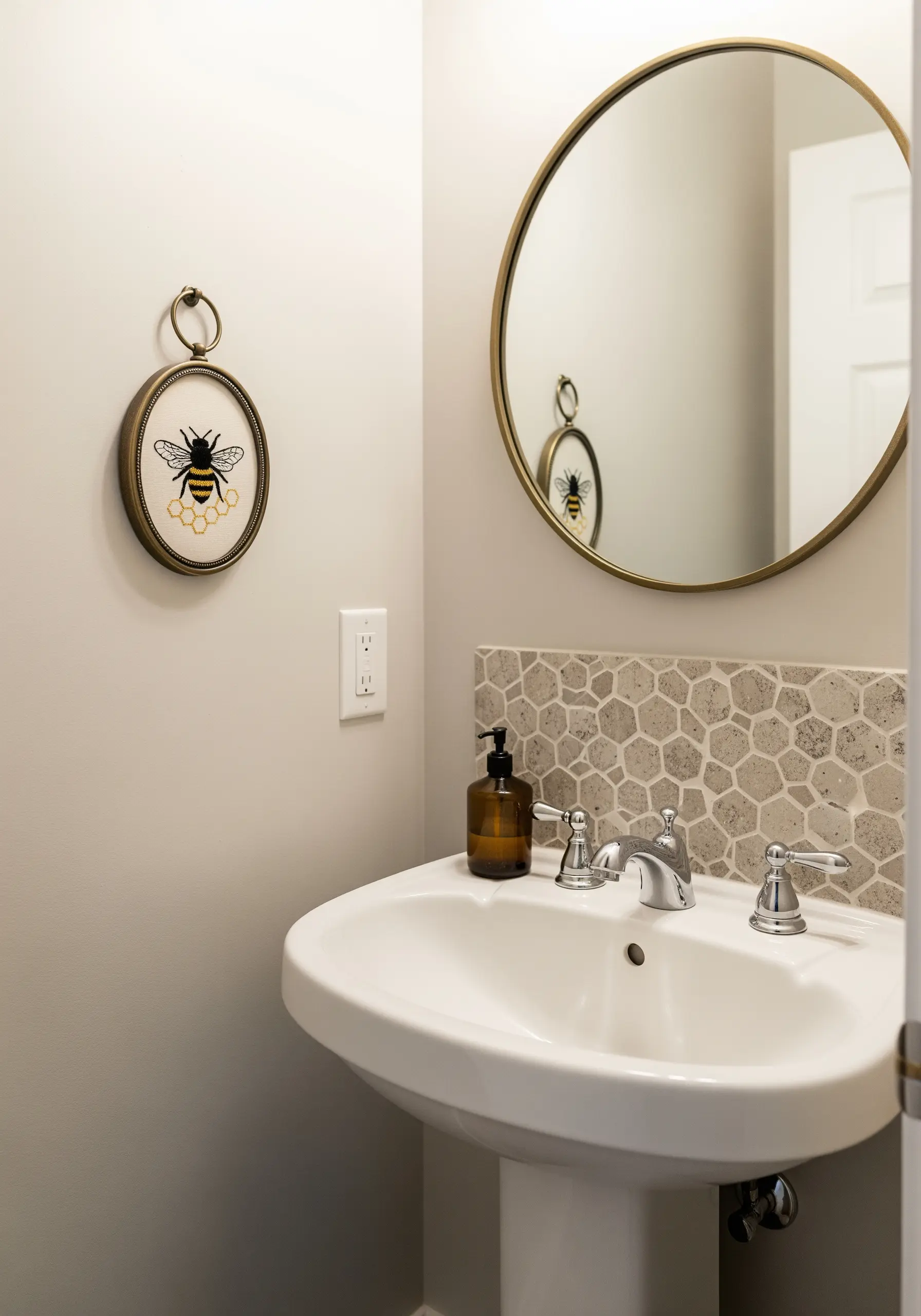 An embroidered bee in a small oval frame hanging in a bathroom.