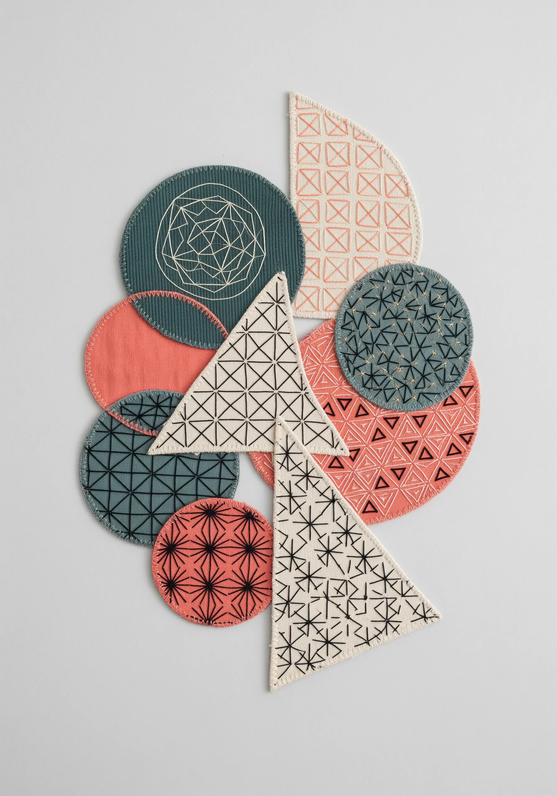 A collage of geometric fabric shapes with embroidered patterns and clean edges.