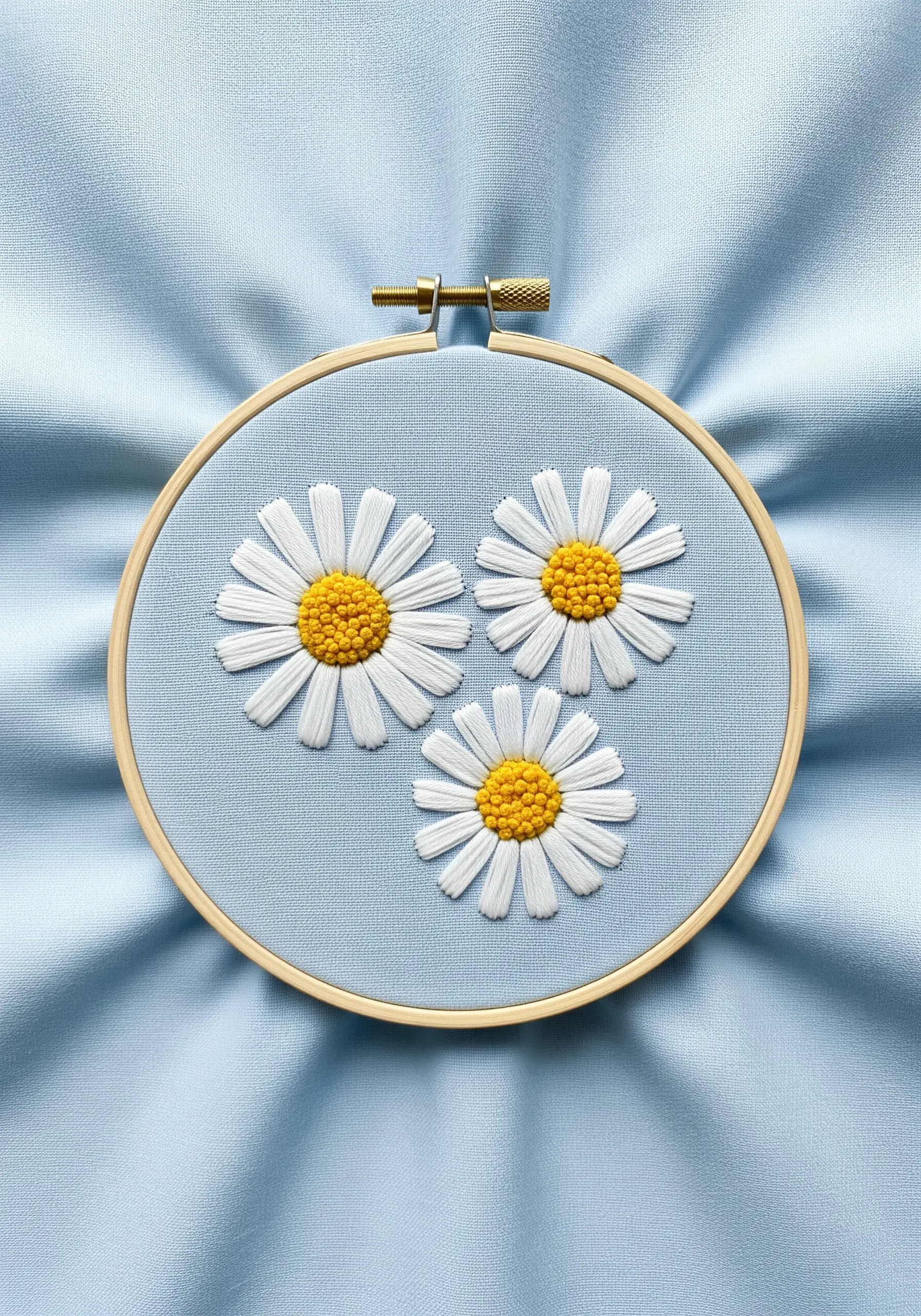 Three daisies with white satin stitch petals and textured yellow centers on blue fabric.