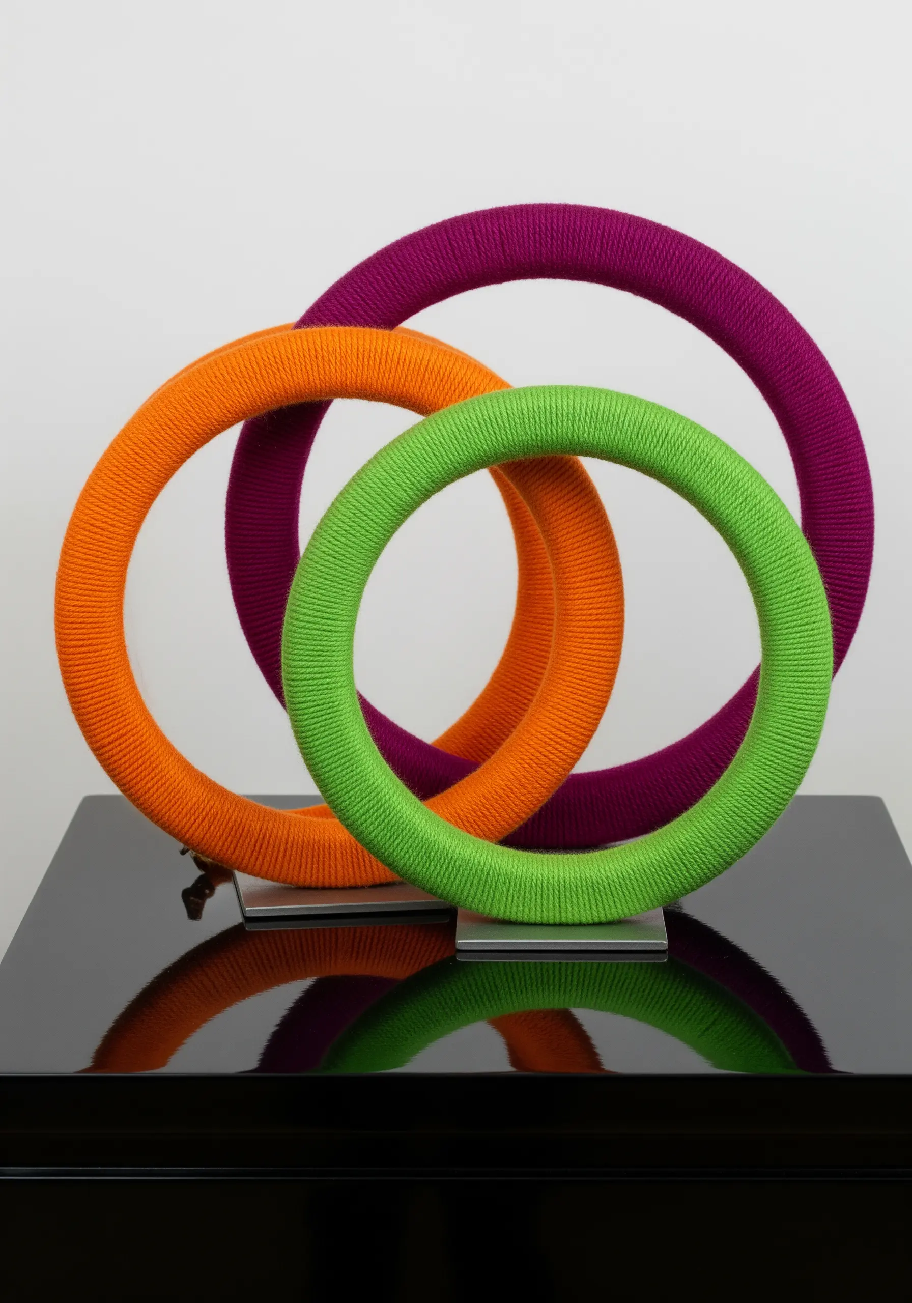 Three interlocking rings wrapped in bright green, orange, and purple yarn, standing as a sculpture.