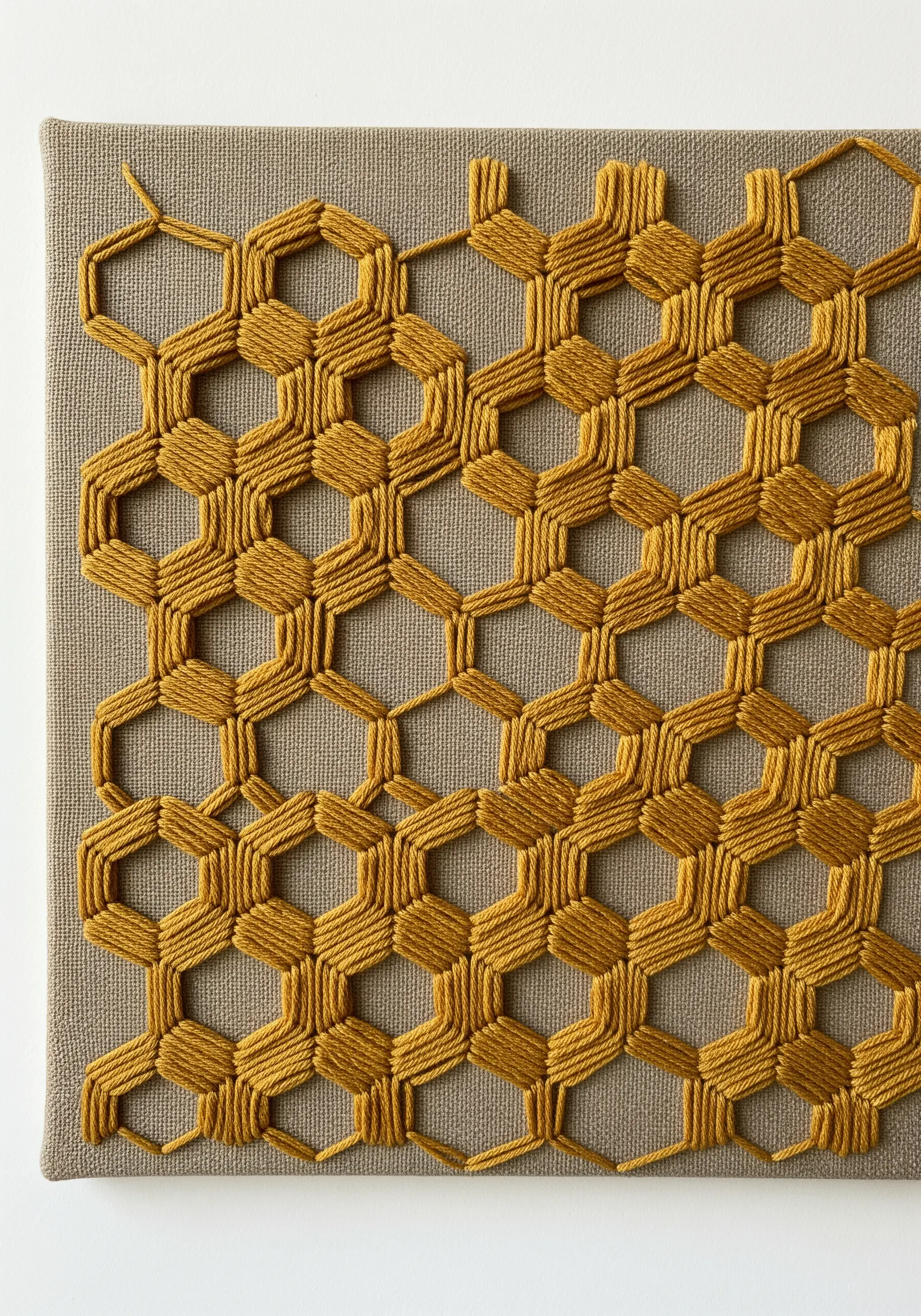 A honeycomb pattern stitched in gold thread, where the empty hexagonal spaces form the design.