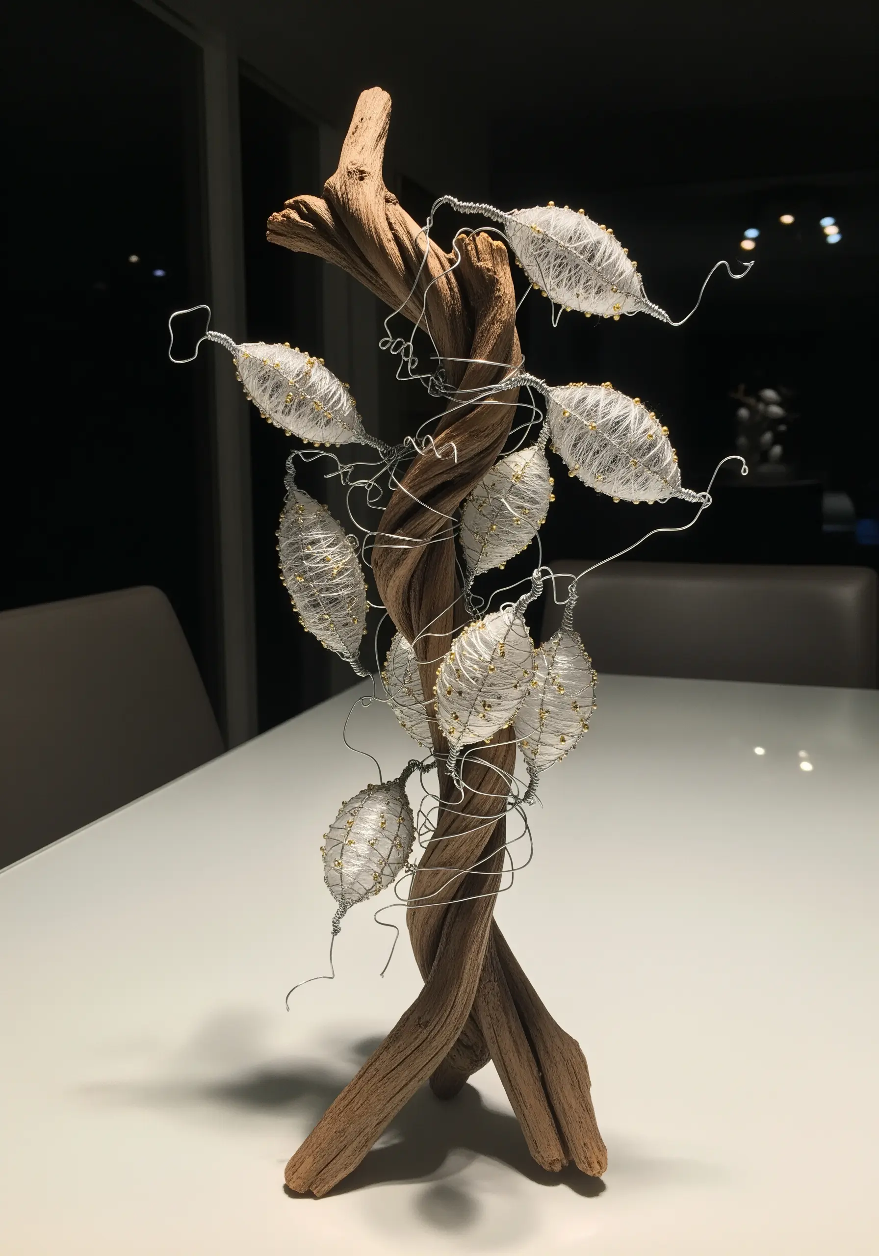 A sculpture made of driftwood with wire-and-thread pods wrapping around it.