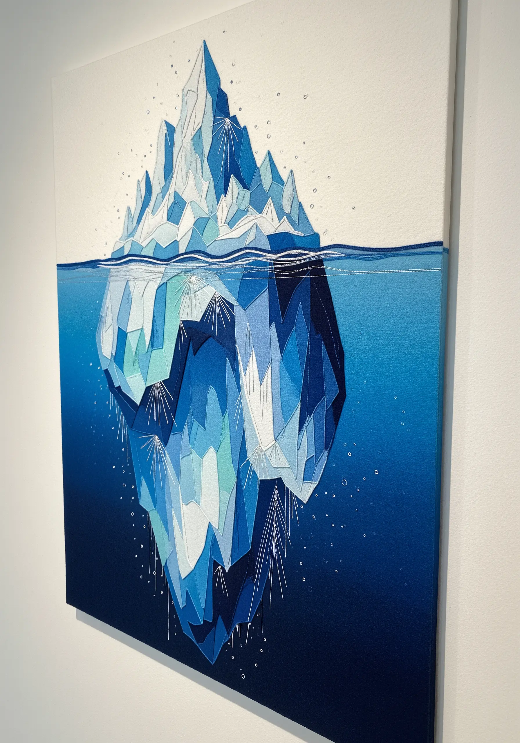 A geometric embroidery of an iceberg, using blocks of satin stitch in various shades of blue.