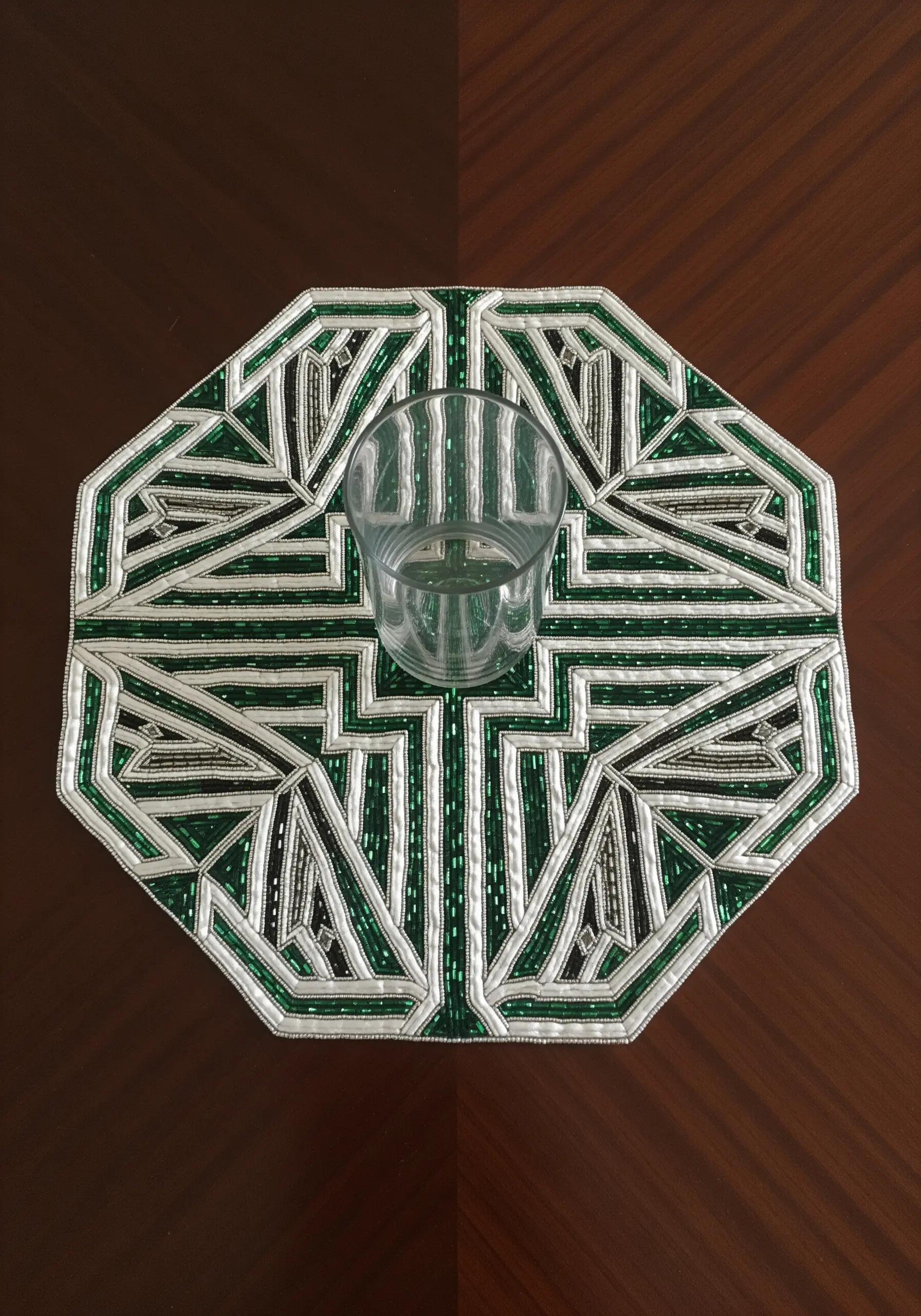 An octagonal placemat with a geometric Art Deco pattern made of green, white, and black beads.