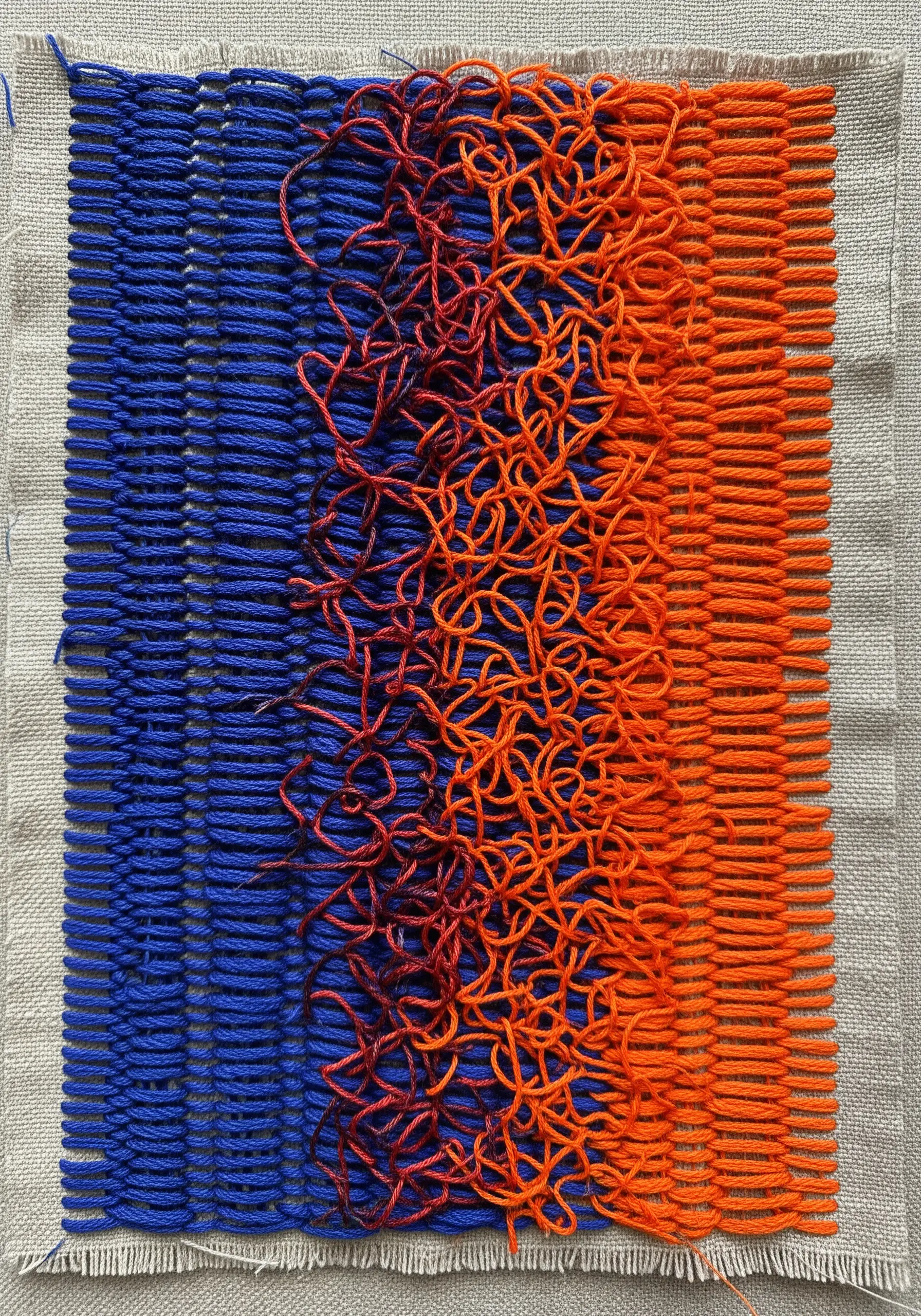 A textile piece with orderly blue vertical stitches on one side and chaotic orange loops on the other