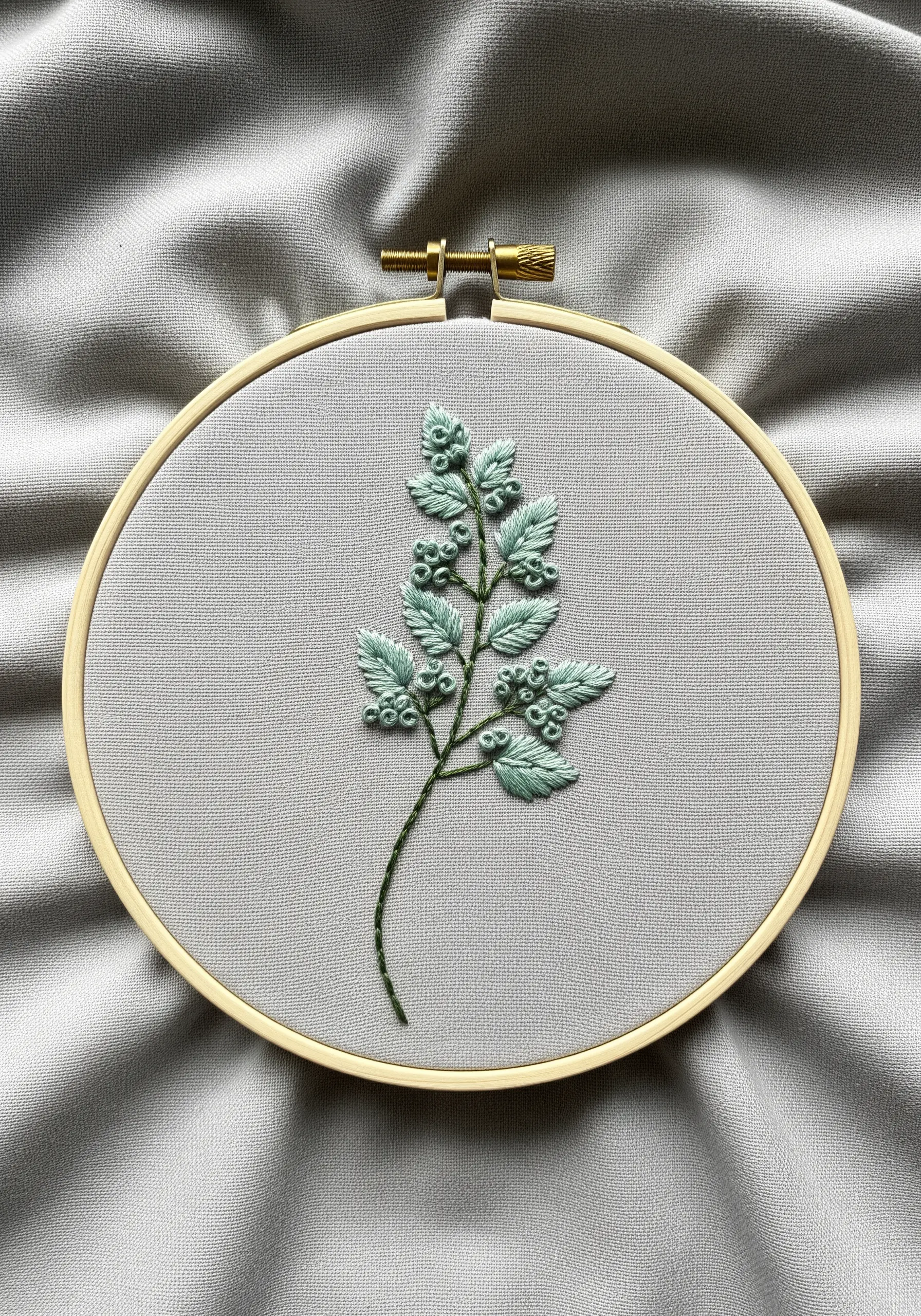 An herb sprig with smooth satin-stitched leaves and clusters of French knot berries in aqua green.