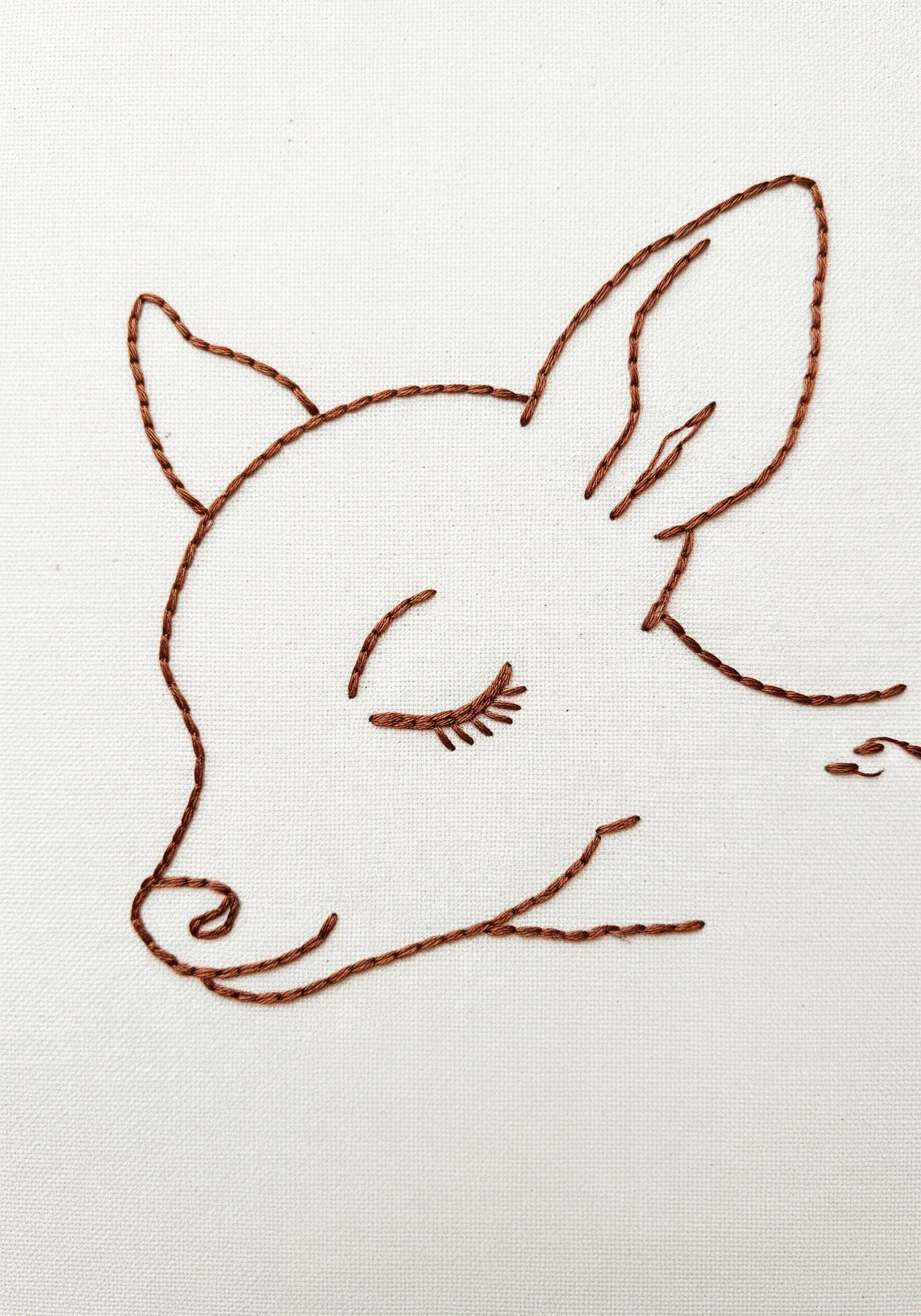 A fawn's head embroidered in a minimalist line-art style using brown backstitch.