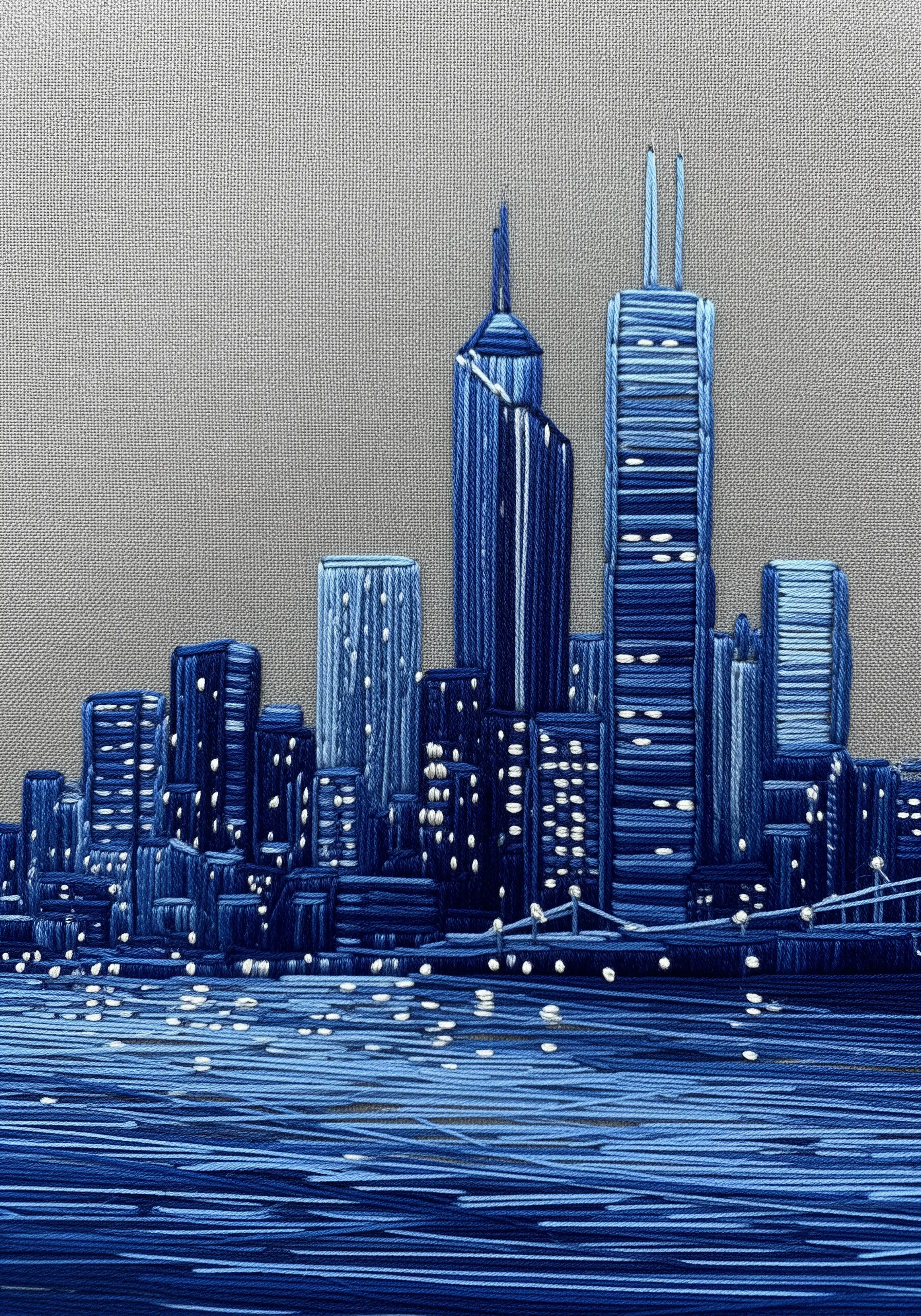 A monochromatic cityscape embroidered in various shades of blue thread.