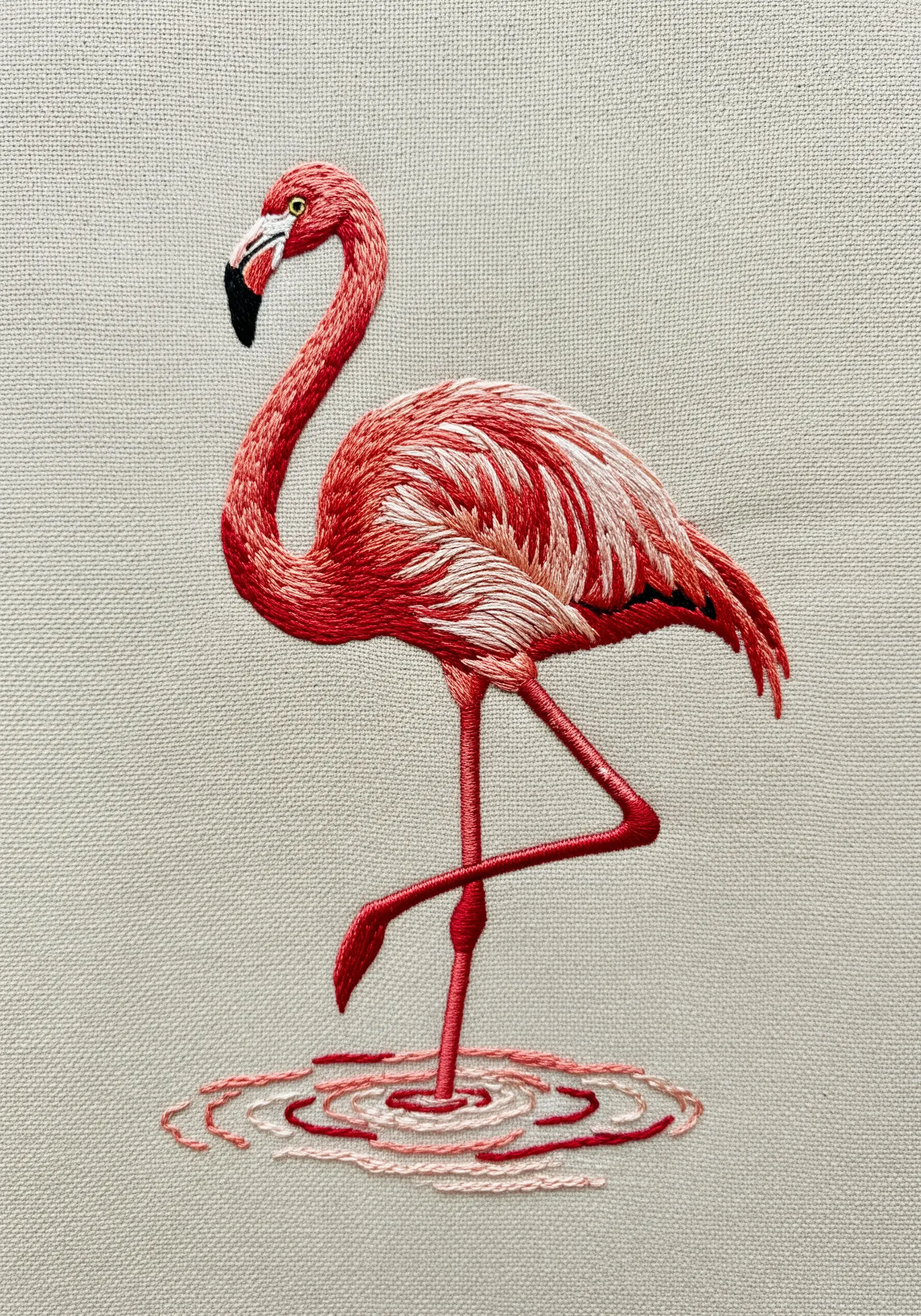 Detailed embroidered flamingo standing in water with concentric line-stitched ripples.