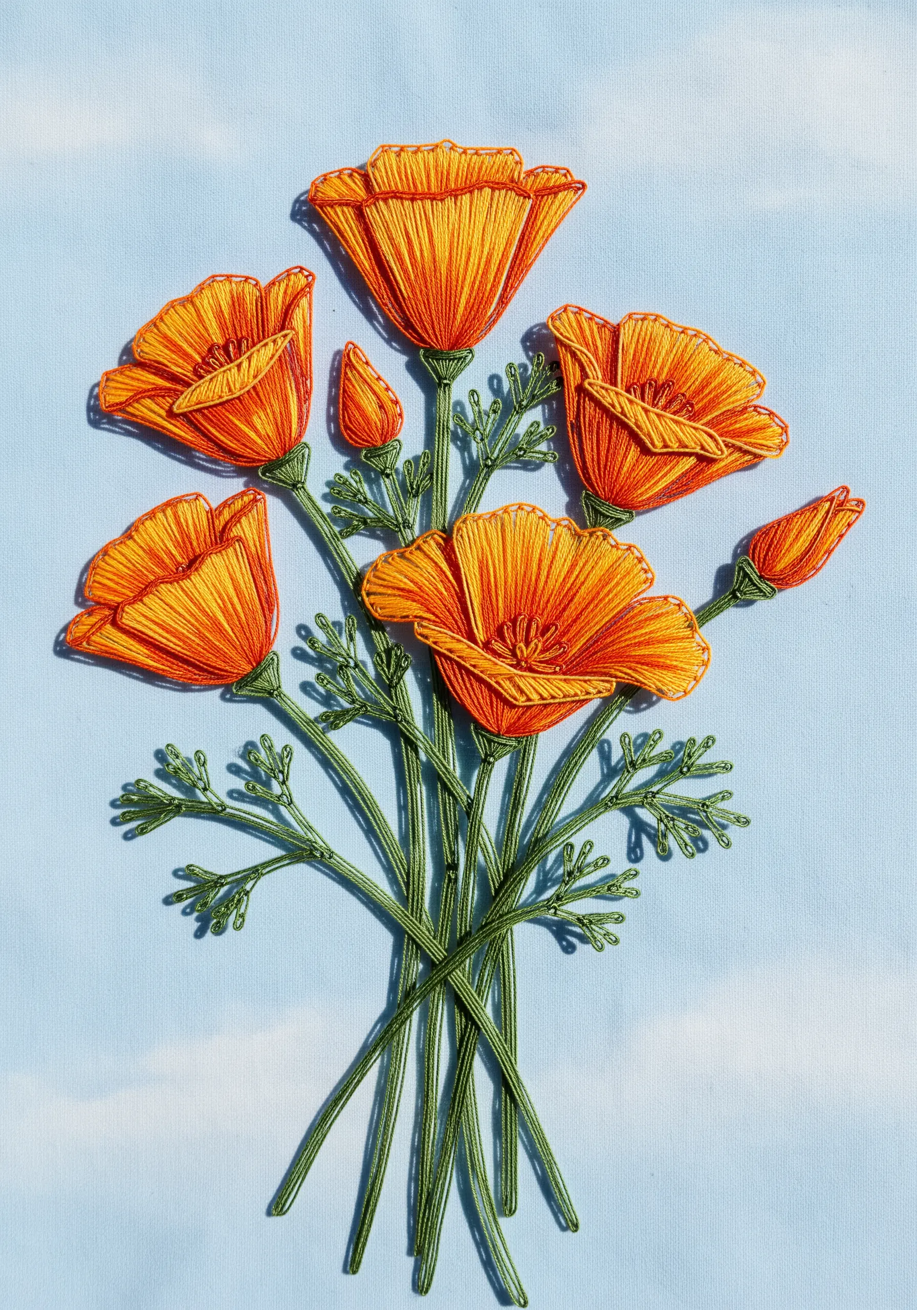 Embroidered orange California poppies with delicate, open stitching on a light blue background.