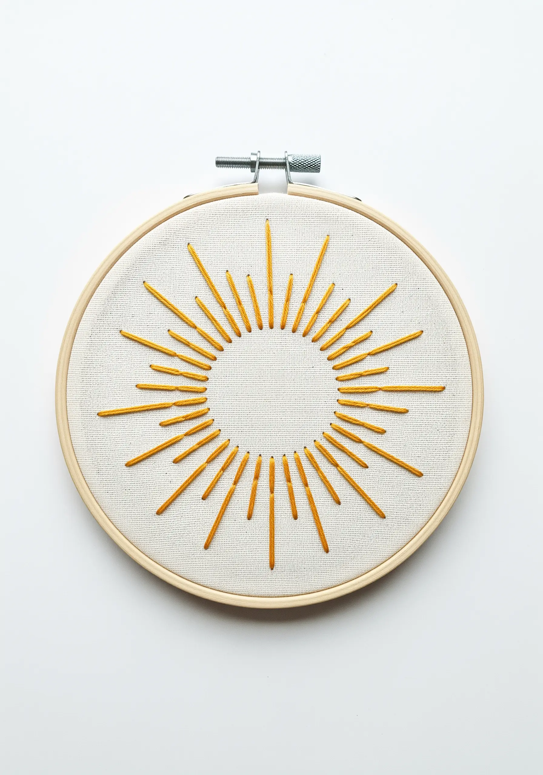 A sunburst motif with radiating yellow straight stitches of varying lengths in a hoop.