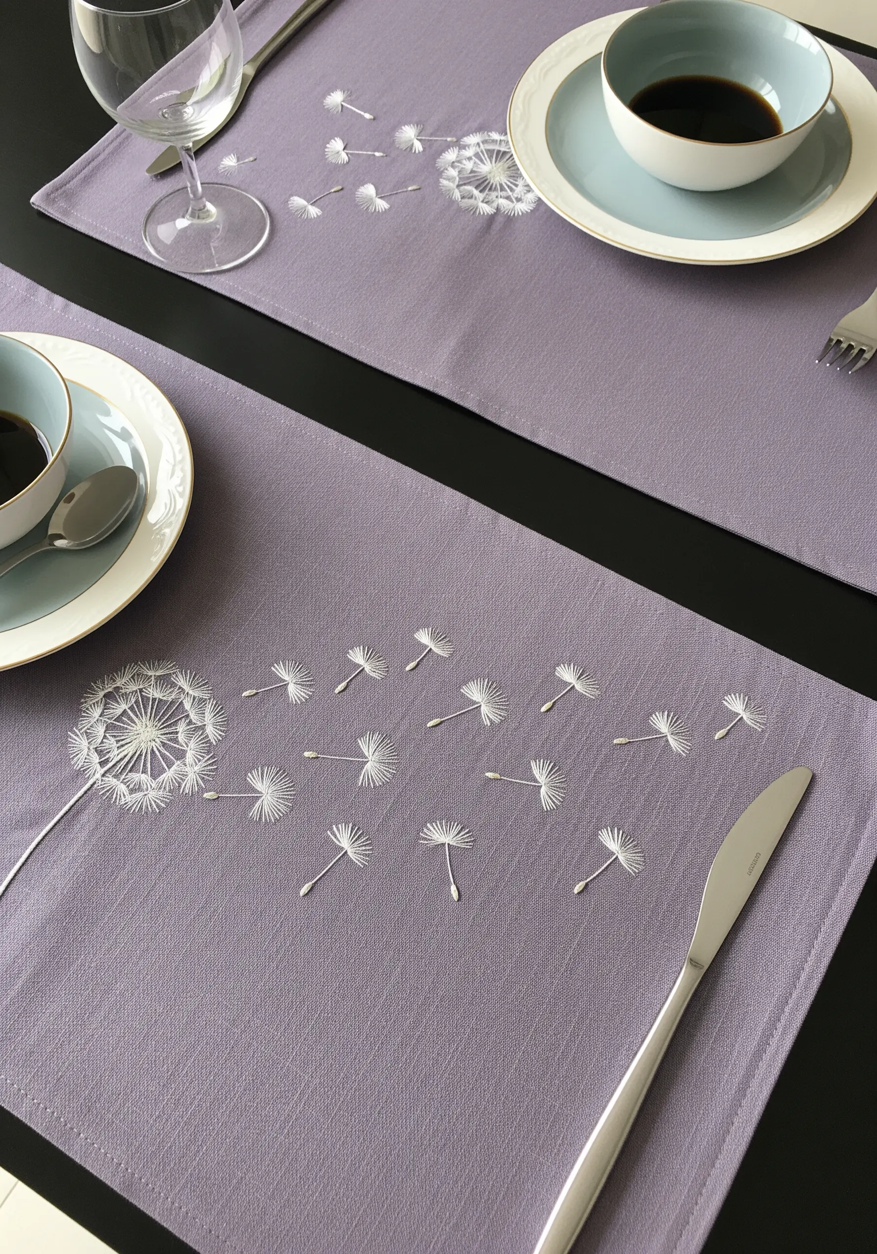A dandelion blowing its seeds across a mauve placemat, all in white thread.