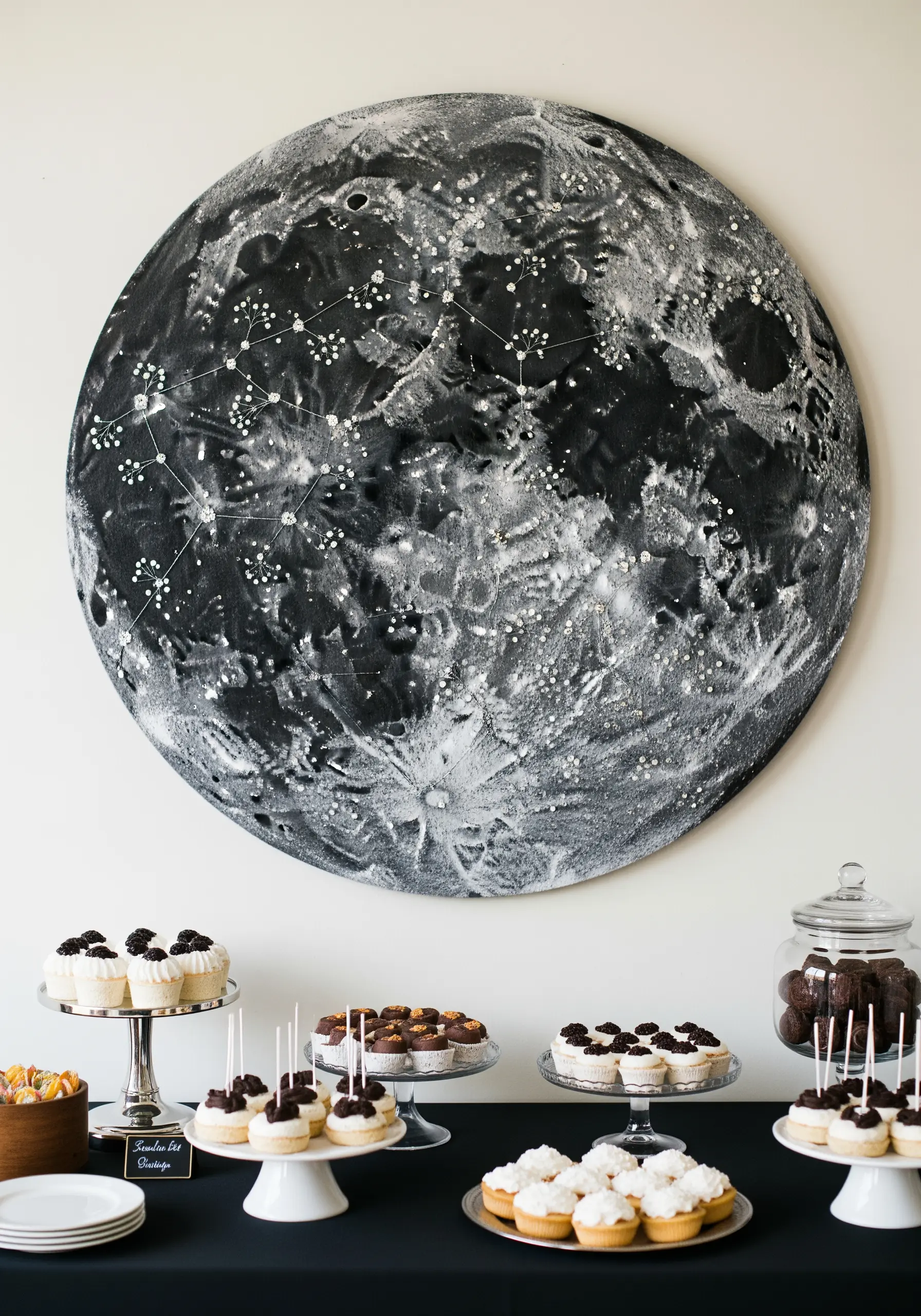 A large, round painted canvas of the moon with embroidered constellations stitched over it.