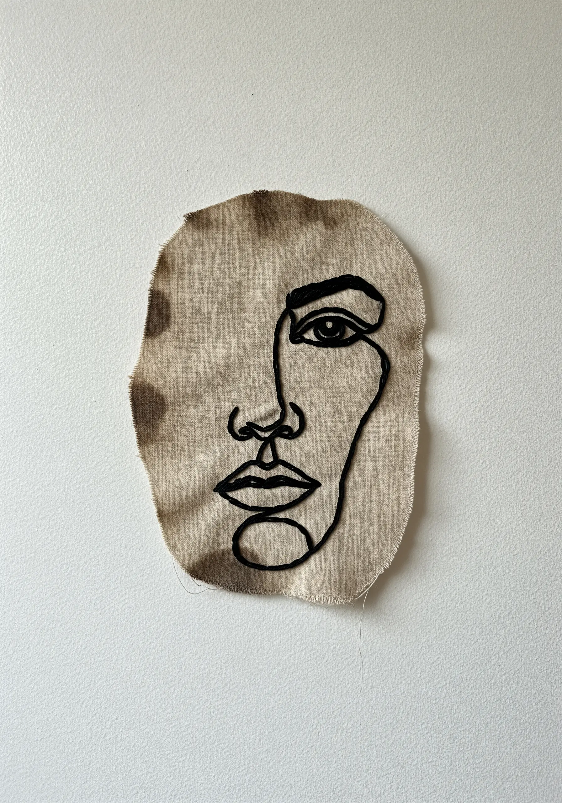 A single-line face portrait created with thick black yarn couched onto a raw-edge fabric scrap.