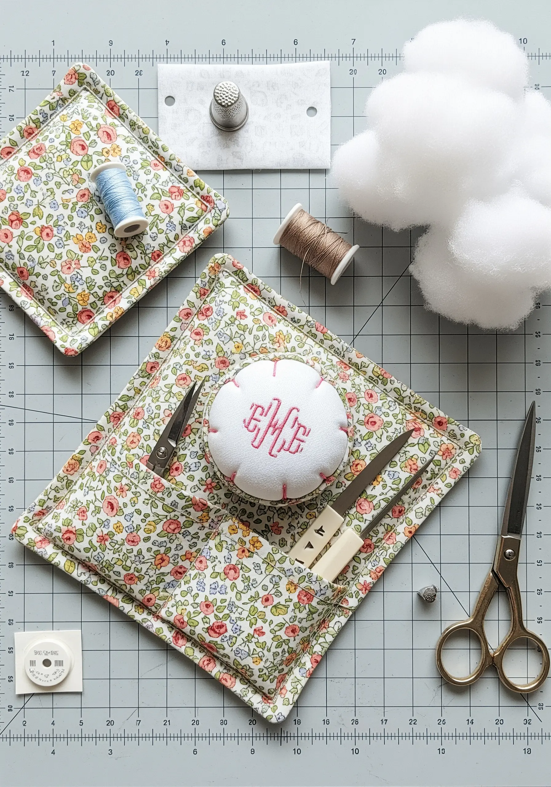 A sewing station with a handmade floral pincushion featuring a pink embroidered monogram.