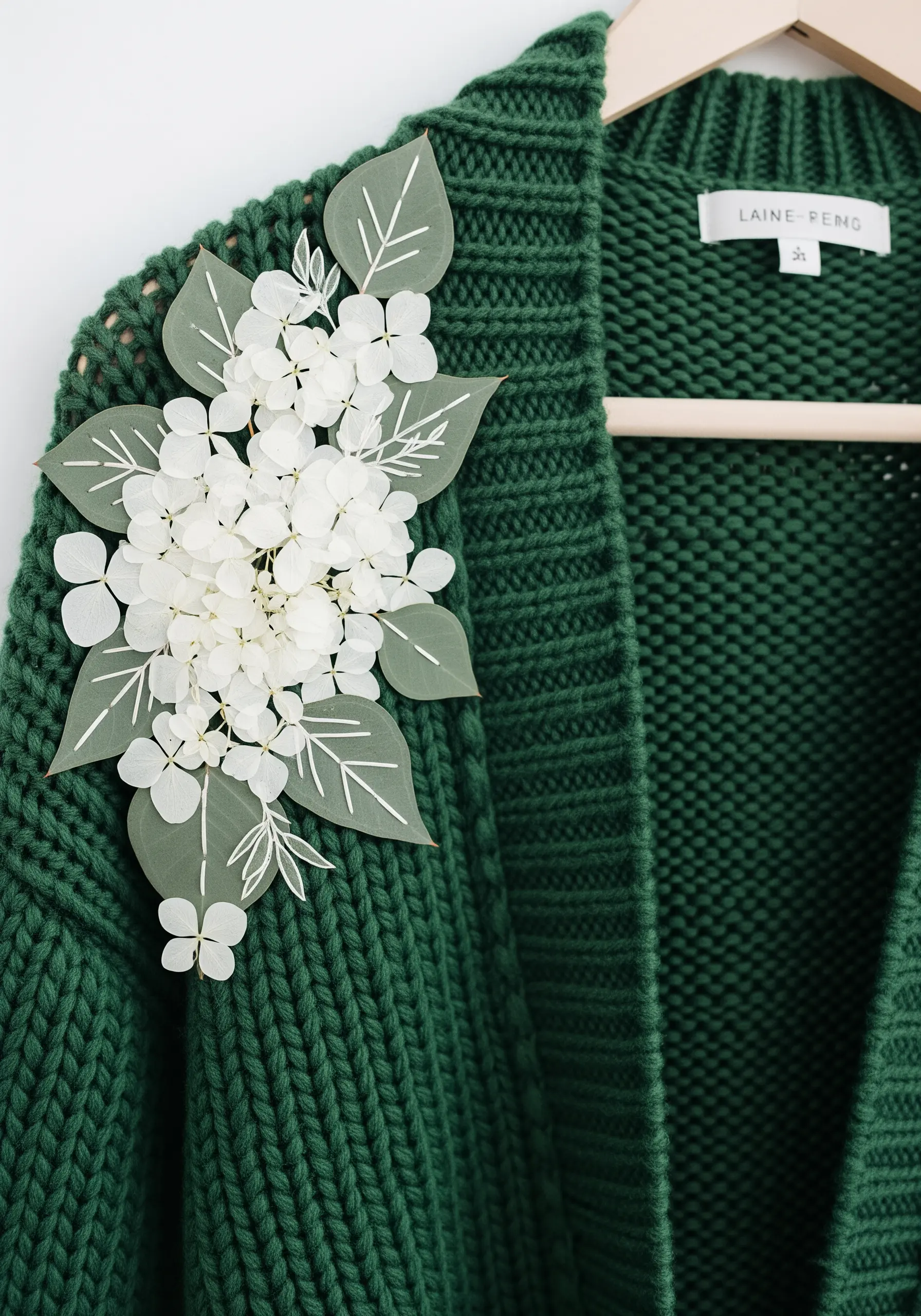 A detachable brooch made of dried hydrangeas and embroidered leaves, pinned to a green knit cardigan.