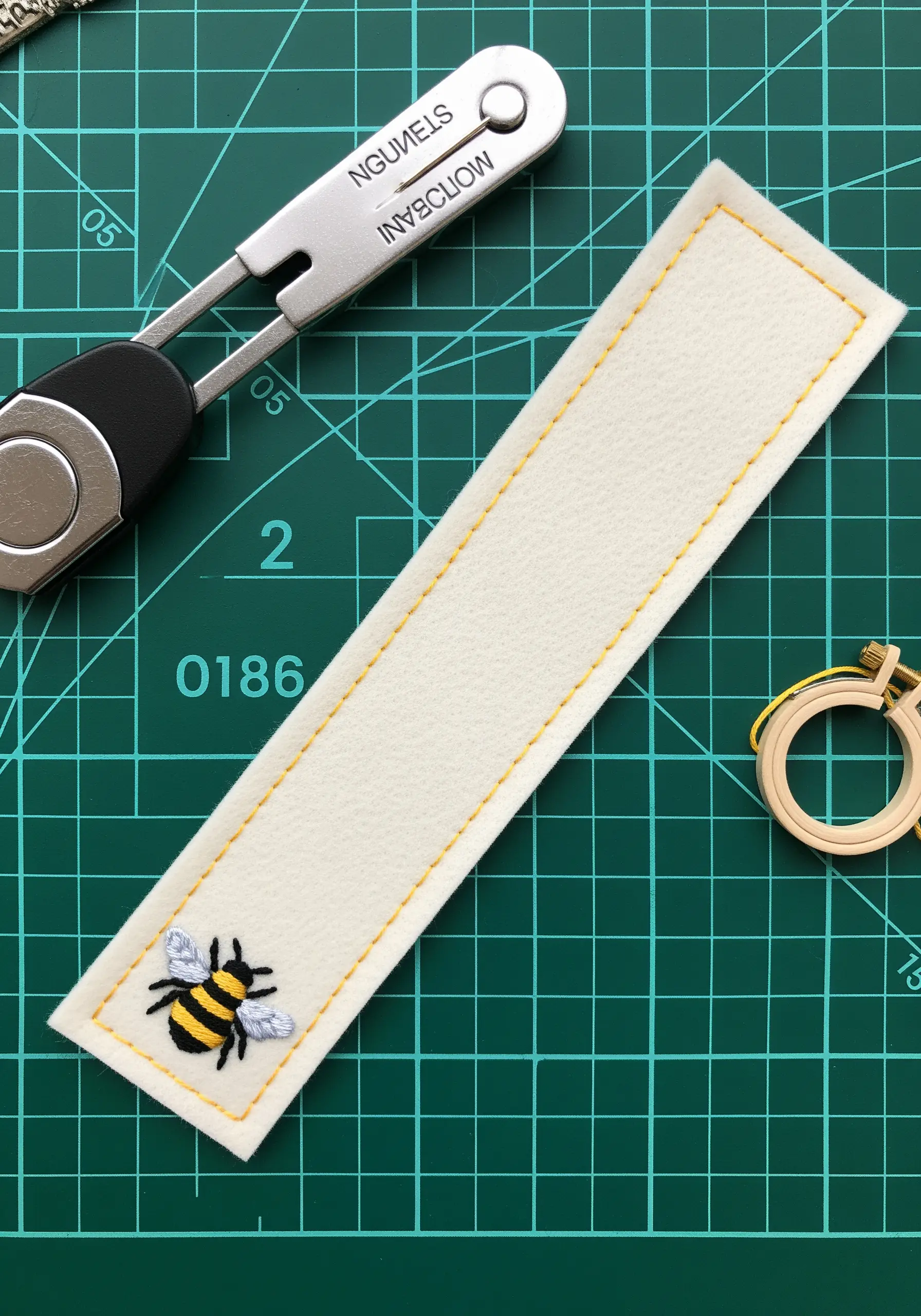 A small white felt bookmark with a tiny embroidered bee motif.