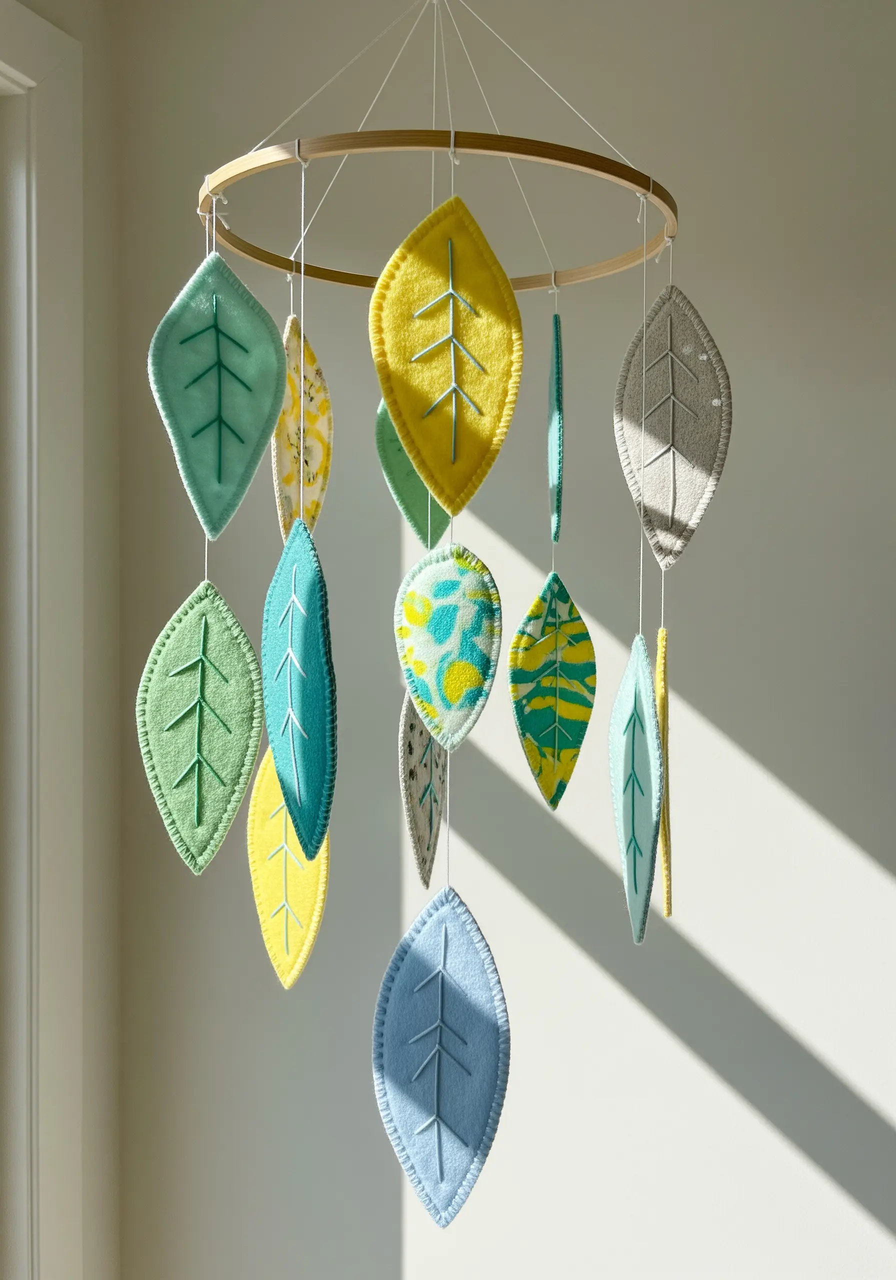 A nursery mobile with hanging felt leaves in various colors, detailed with embroidered veins.