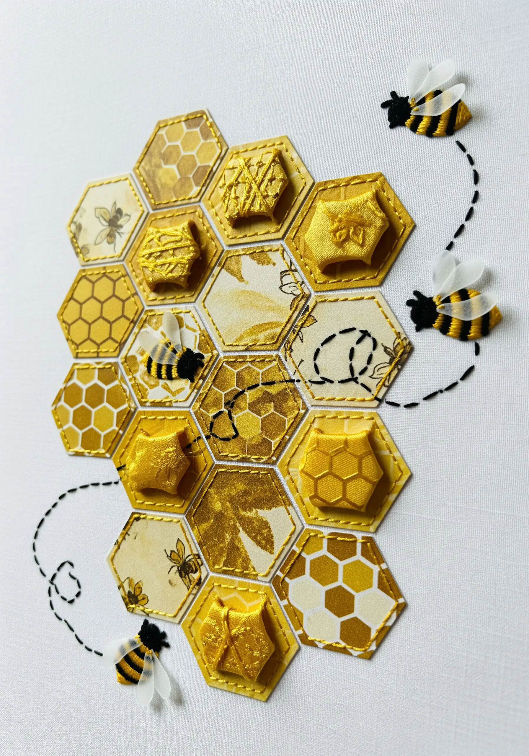 A honeycomb design made of paper and fabric hexagons, with small 3D embroidered bees.
