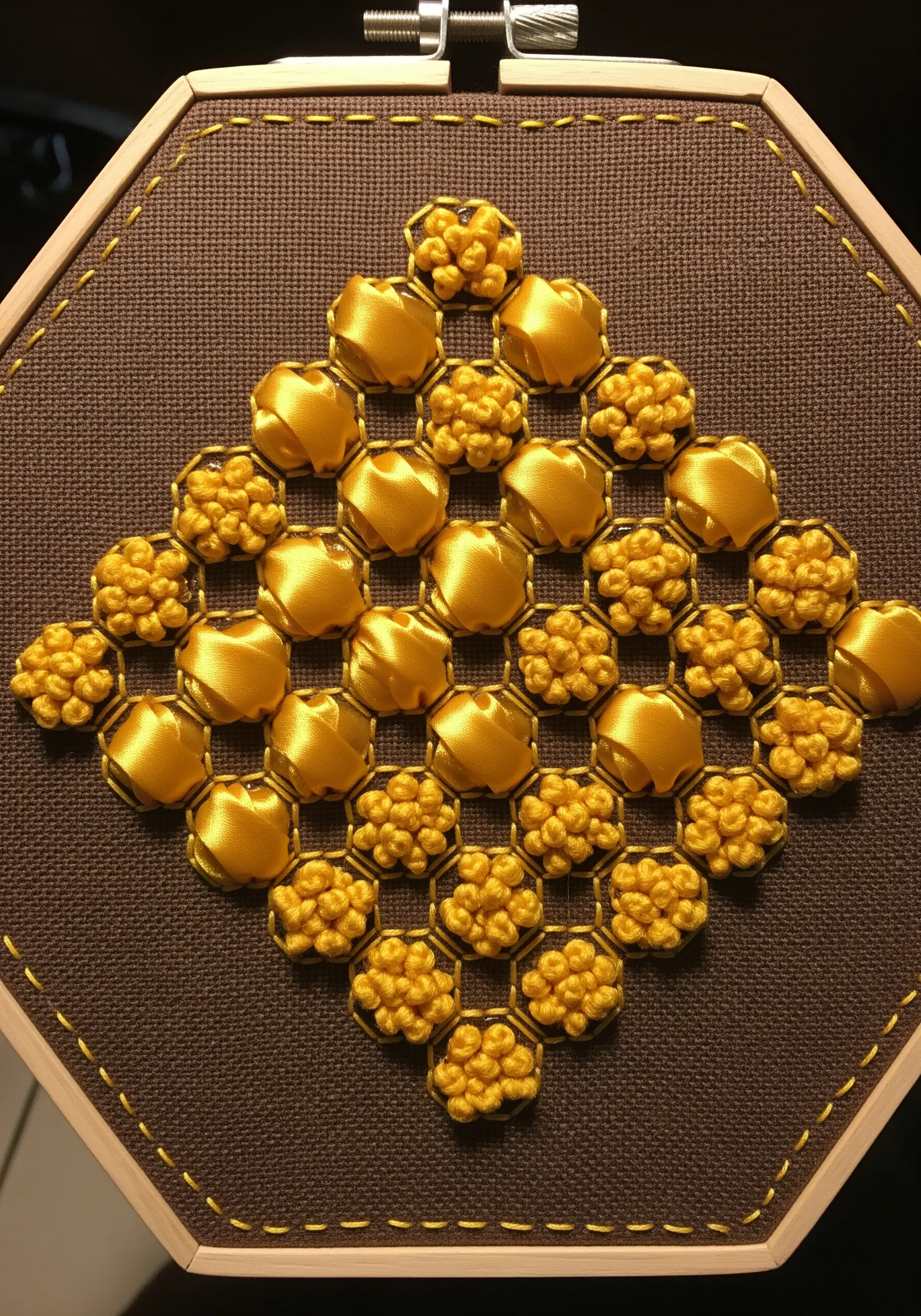 A honeycomb pattern in an octagonal hoop, made with folded yellow ribbon and textured French knots.