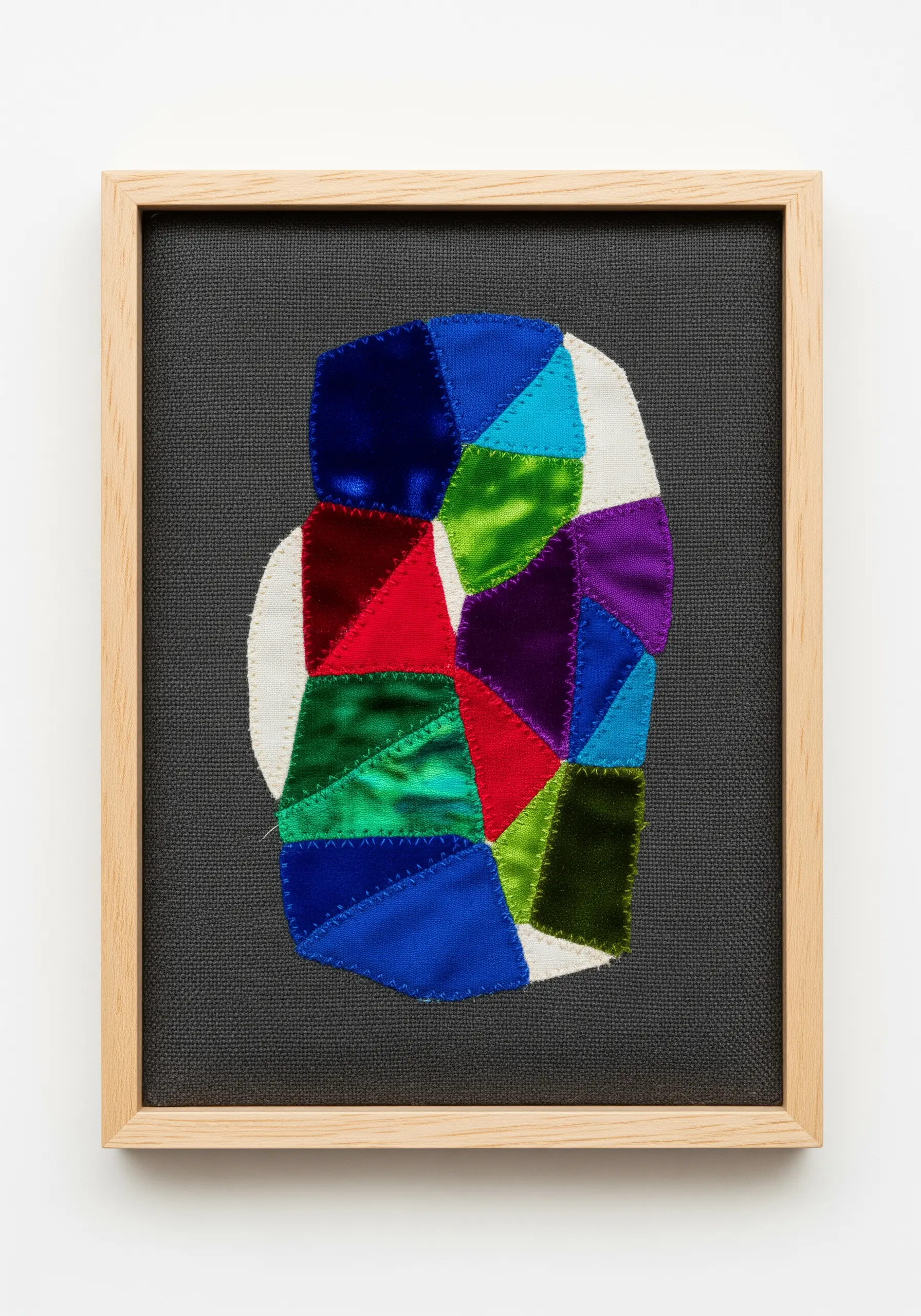 An abstract framed artwork made of colorful, geometric scraps of velvet and satin.