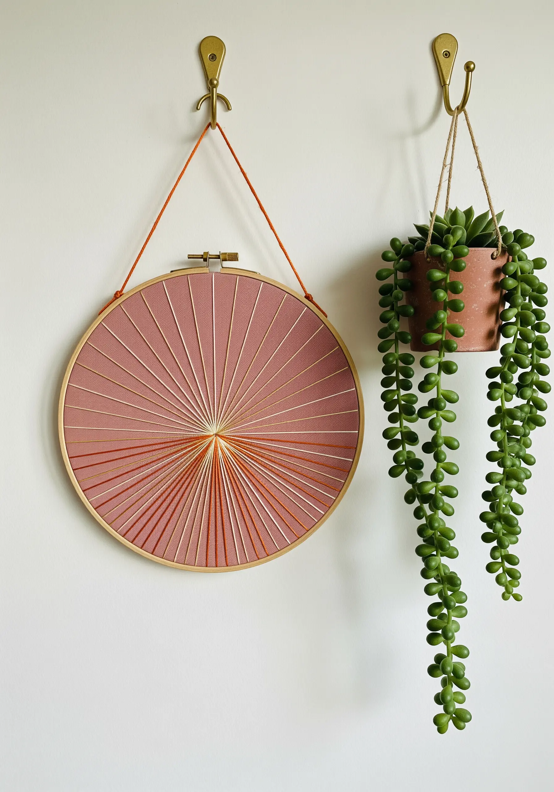 A sunburst string art design inside an embroidery hoop using orange threads.