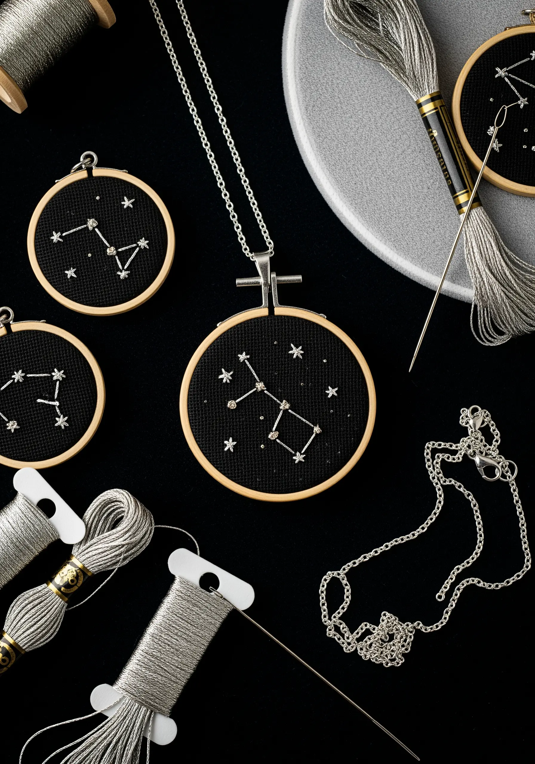 Miniature embroidery hoop pendants featuring silver-stitched constellations on black fabric.