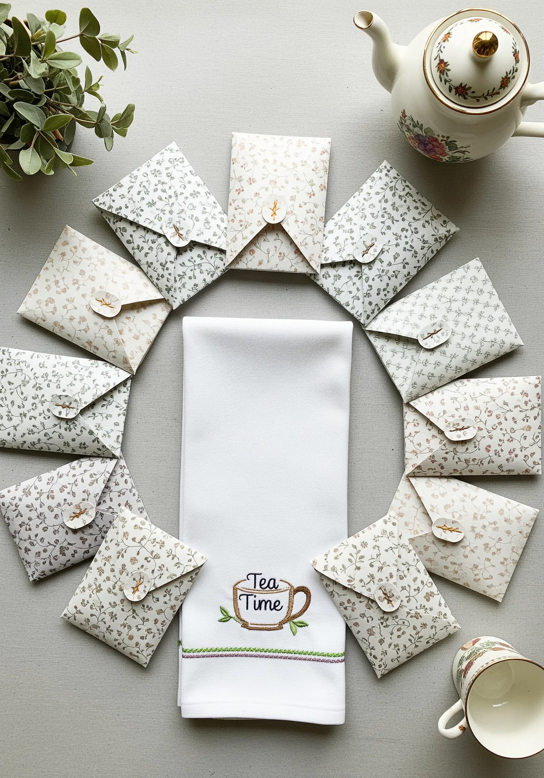 An embroidered 'Tea Time' towel surrounded by small, patterned paper envelopes for tea bags.