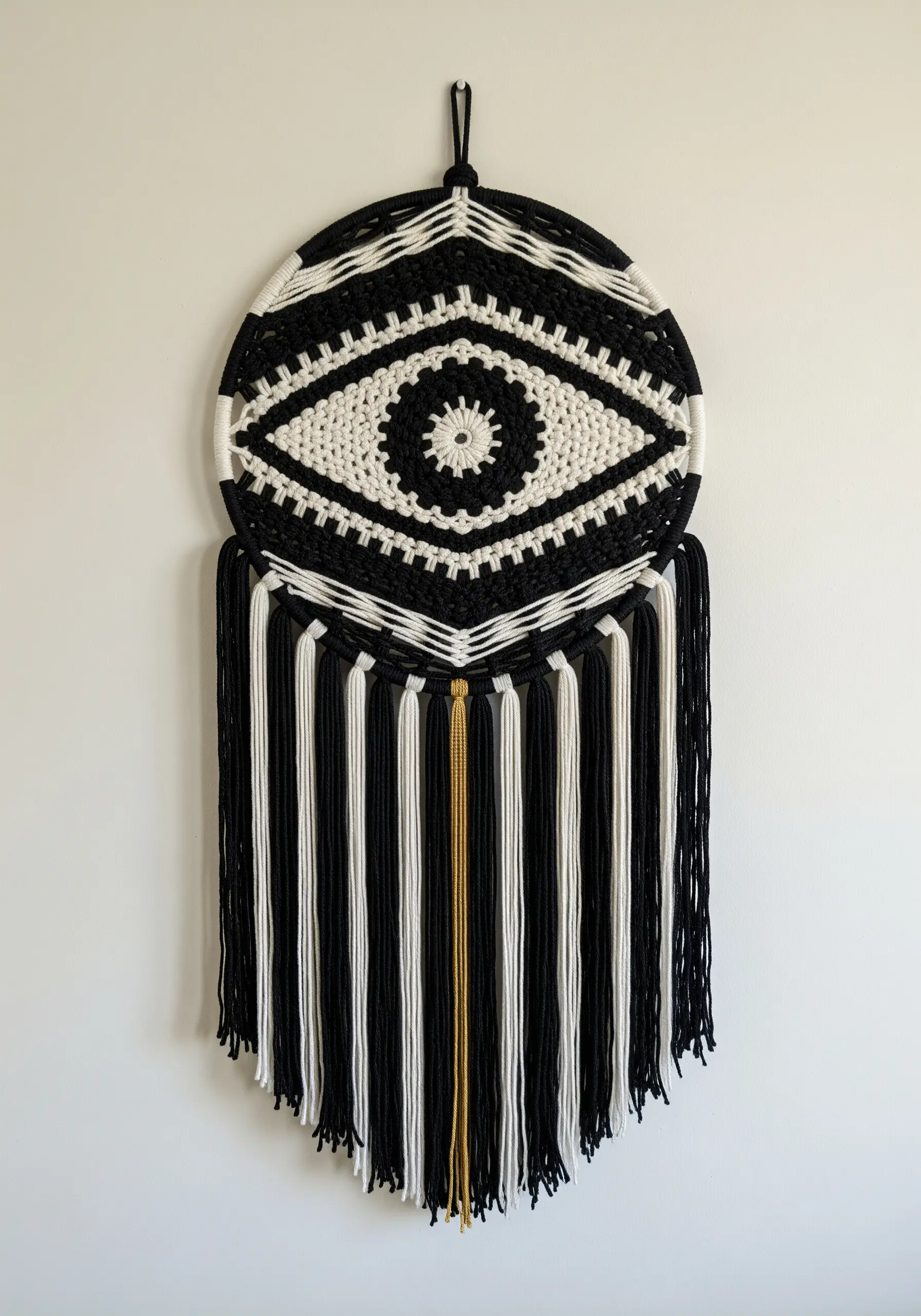A large macrame eye in black and white, with a single gold thread detail.
