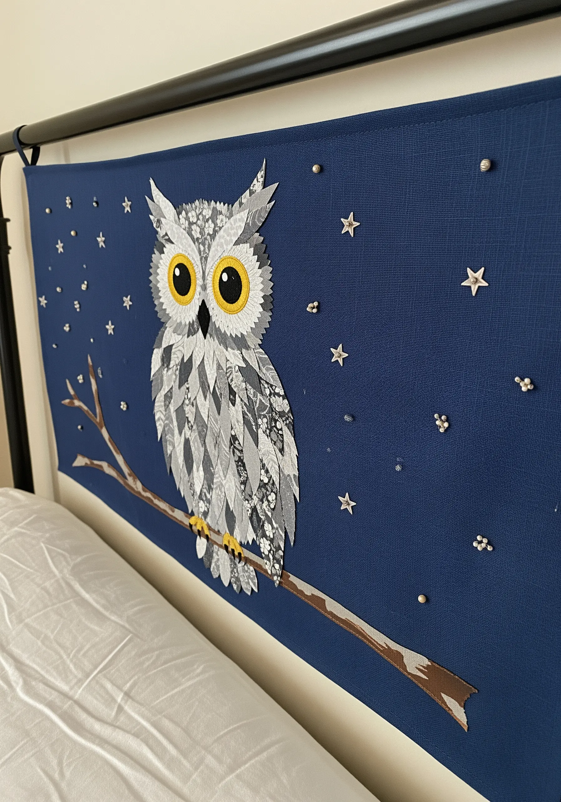 Large owl appliqué made from patterned fabrics on a blue headboard.
