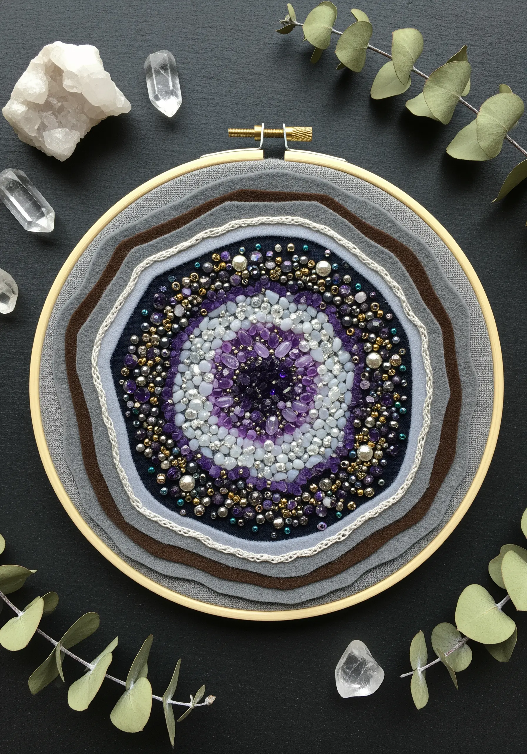An embroidery hoop filled with layered felt and a dense center of purple and white beads, resembling a geode.