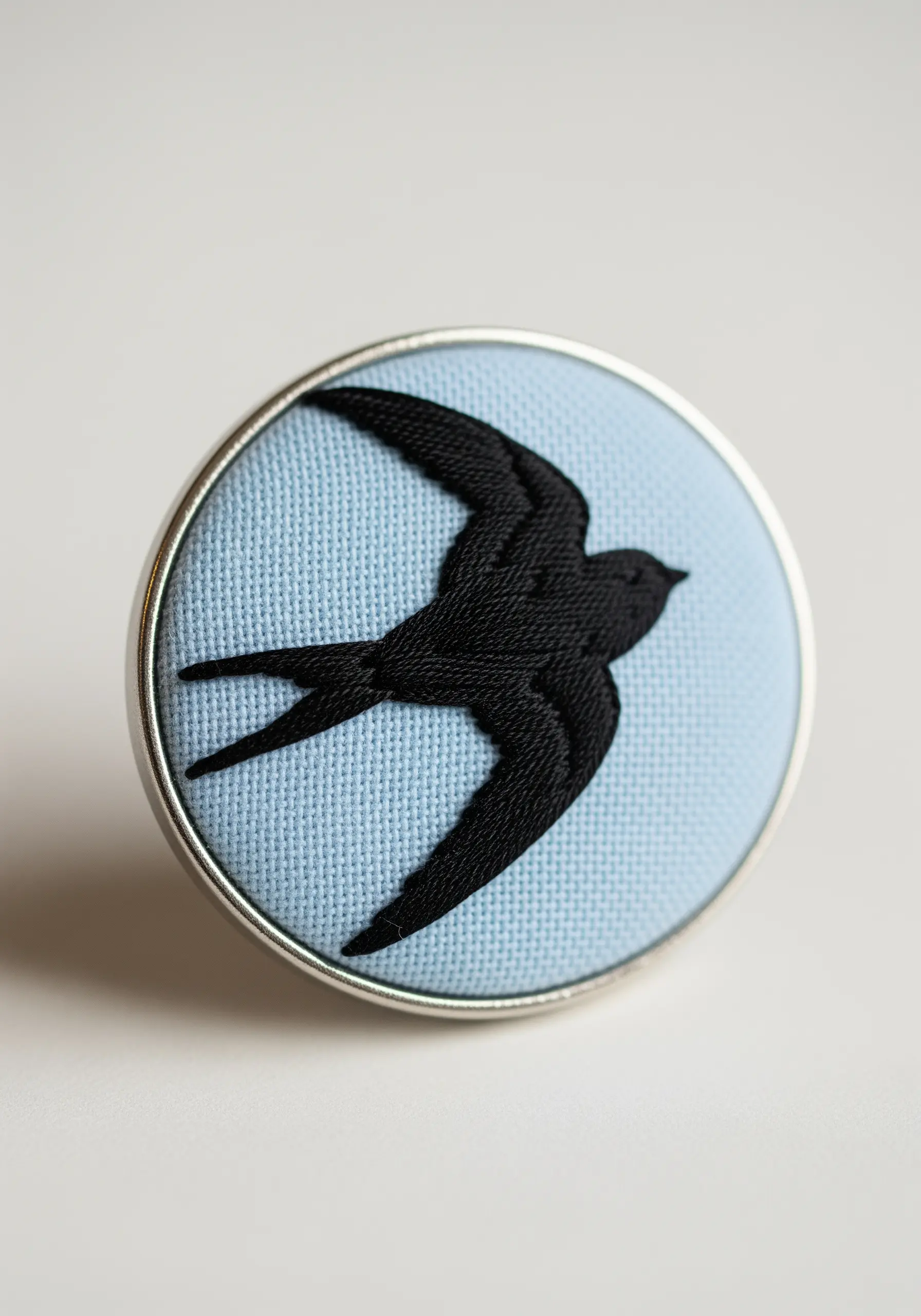 A solid black embroidered silhouette of a swallow in flight on a light blue background.