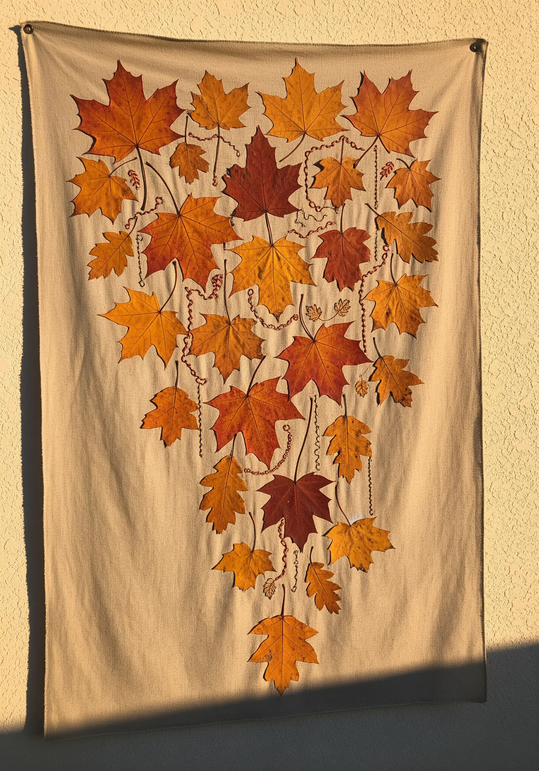 A wall hanging with pressed autumn leaves connected by decorative embroidered lines.