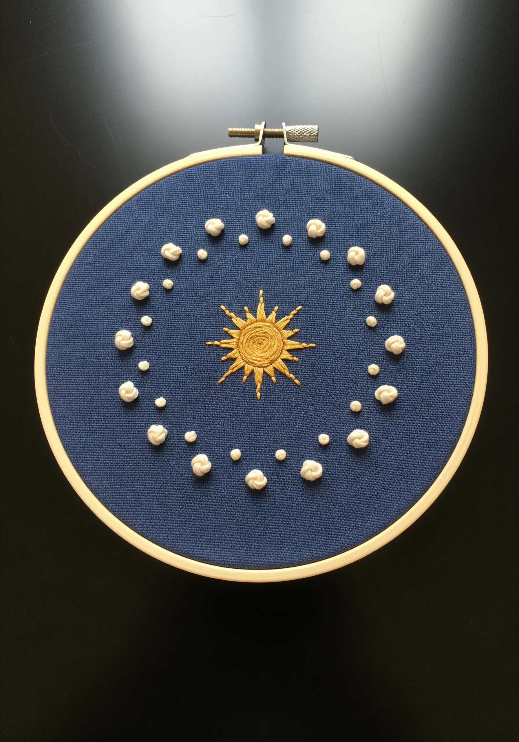 A gold sun surrounded by white knot-stitch stars on dark blue fabric.