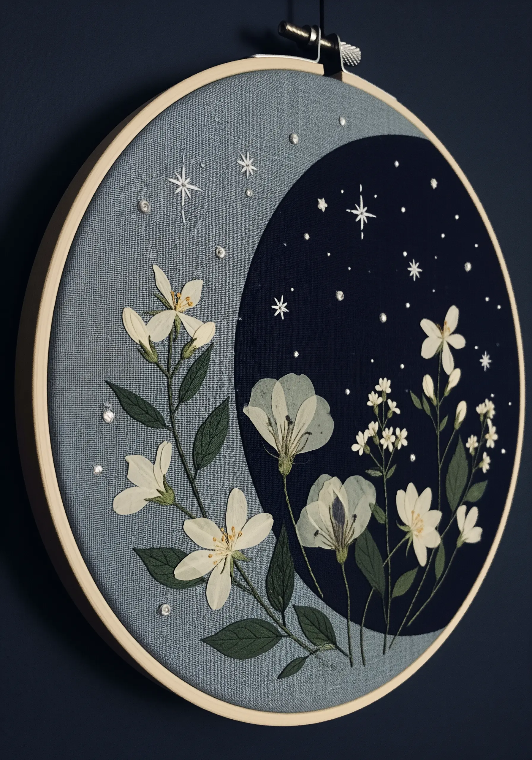 A celestial embroidery hoop with a fabric moon, pressed white flowers, and beaded stars.