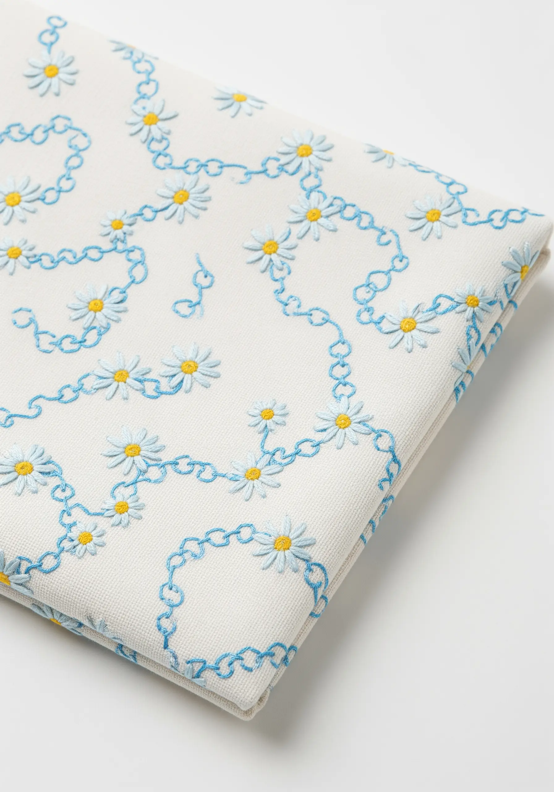 A repeating pattern of tiny daisies connected by light blue embroidered chains on white fabric.