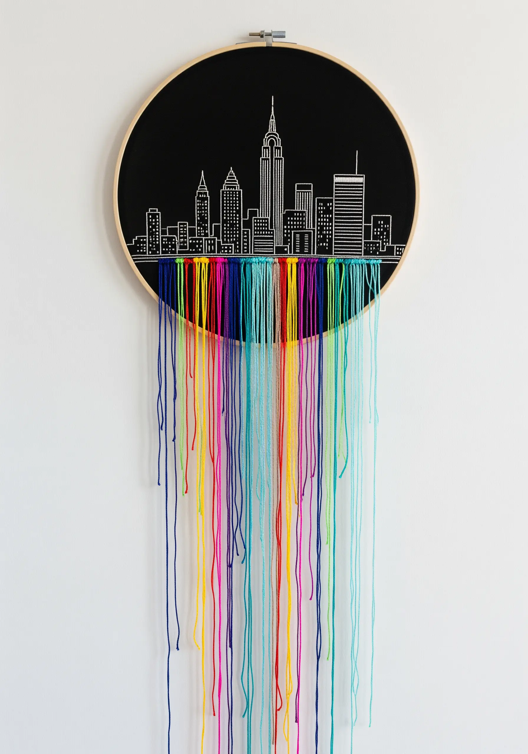 Minimalist white outline of a city on black fabric, with long, colorful threads dripping down.