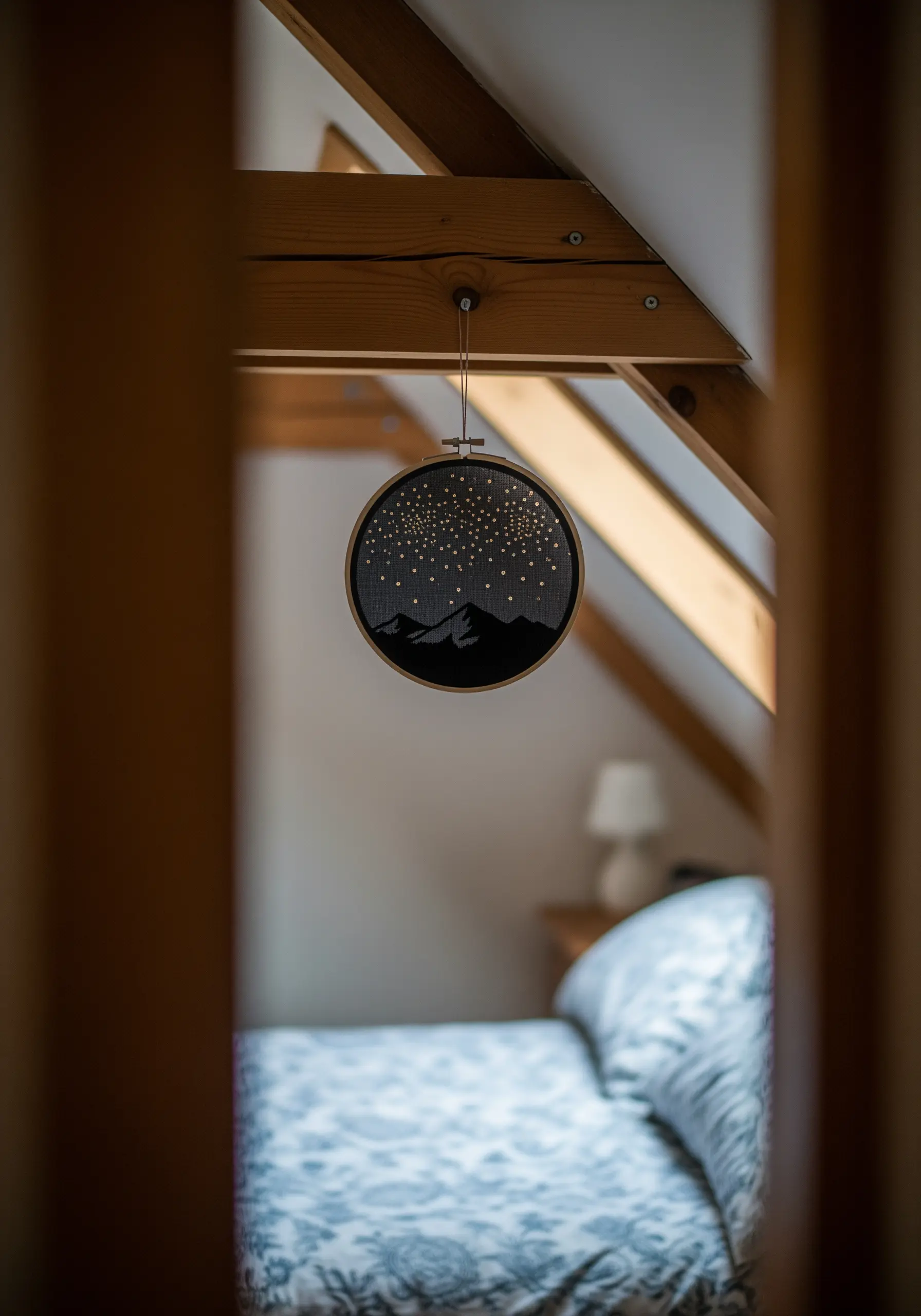 Embroidery of a starry night sky over dark mountain silhouettes in an attic room.