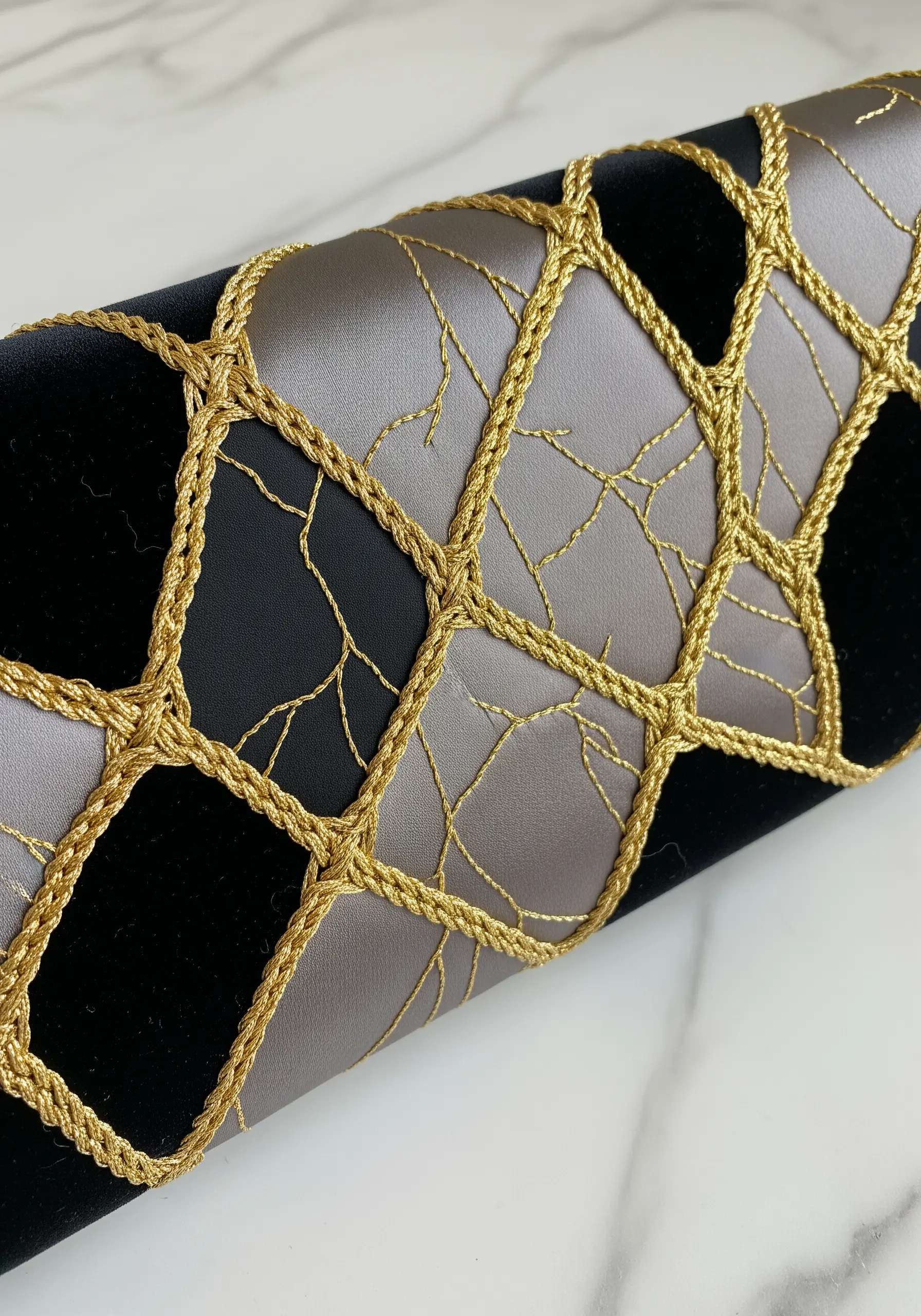 Close-up of black velvet and grey satin with a couched gold cord grid and fine gold stitched veins.