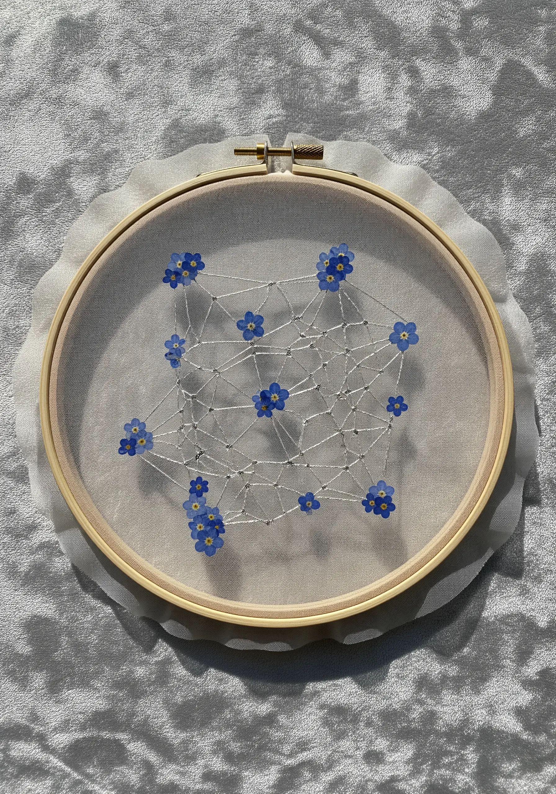 Pressed blue forget-me-nots arranged on sheer organza and connected by a delicate web of white thread.